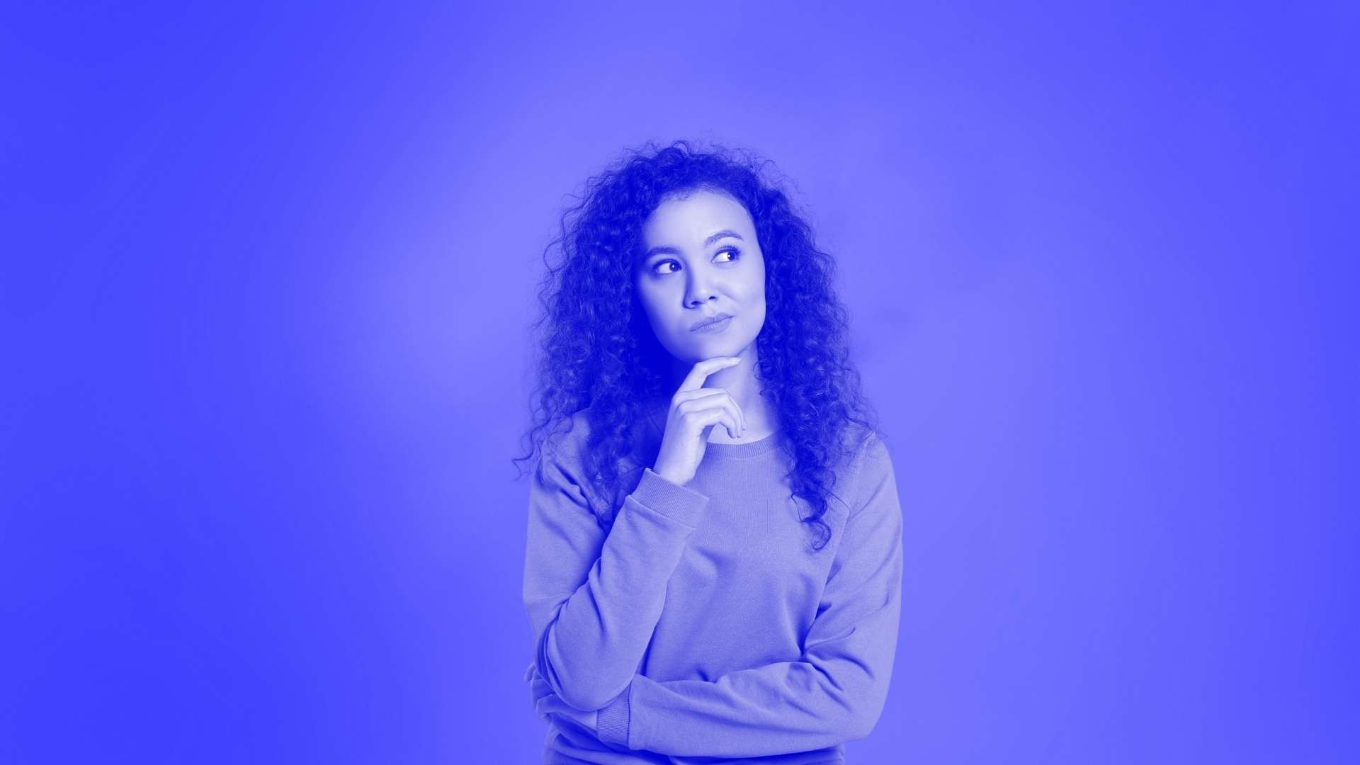 woman with long hair looking pensive with her finger on her chin