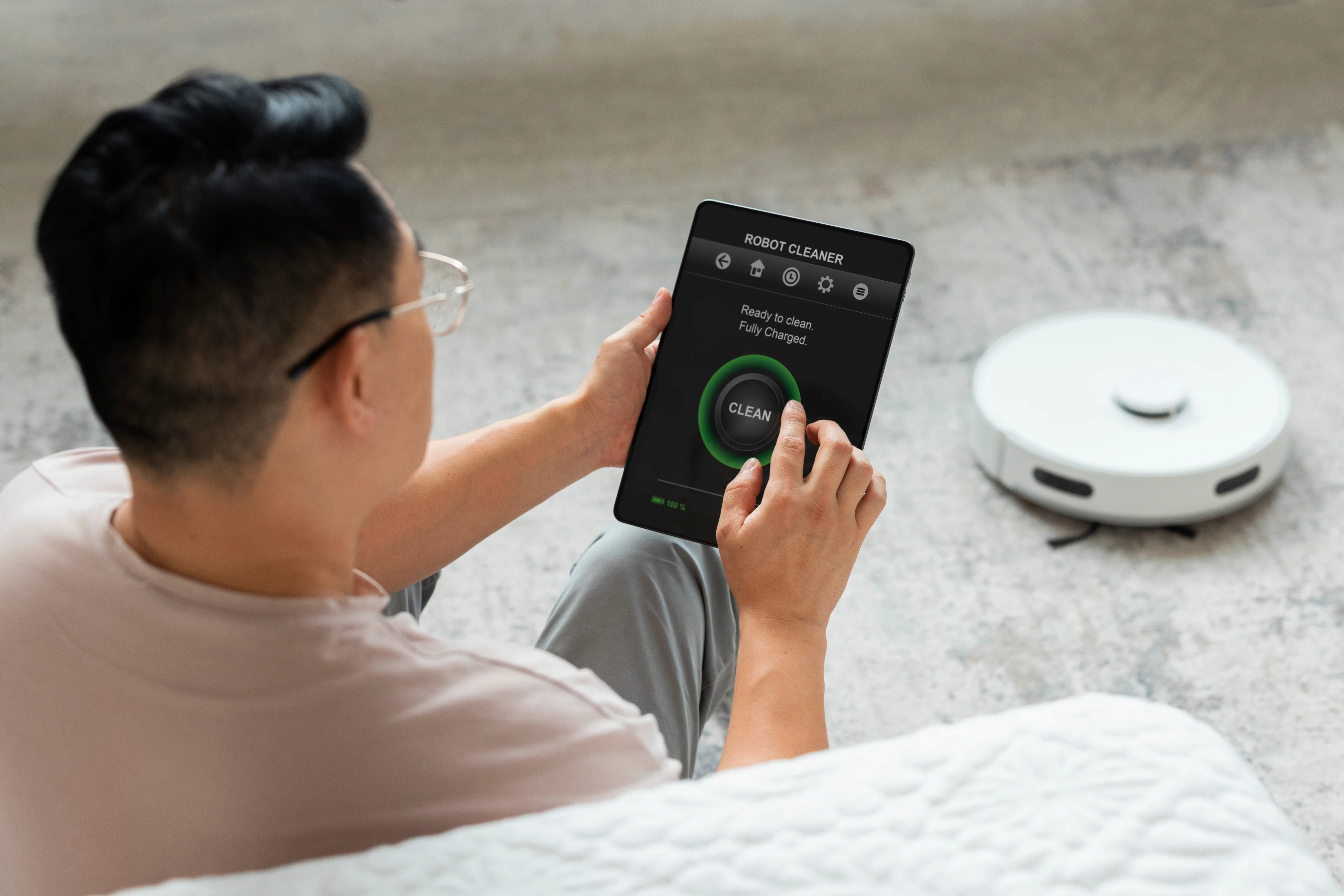 Overhead view of a person using a mobile phone app near a white robot vacuum cleaner.