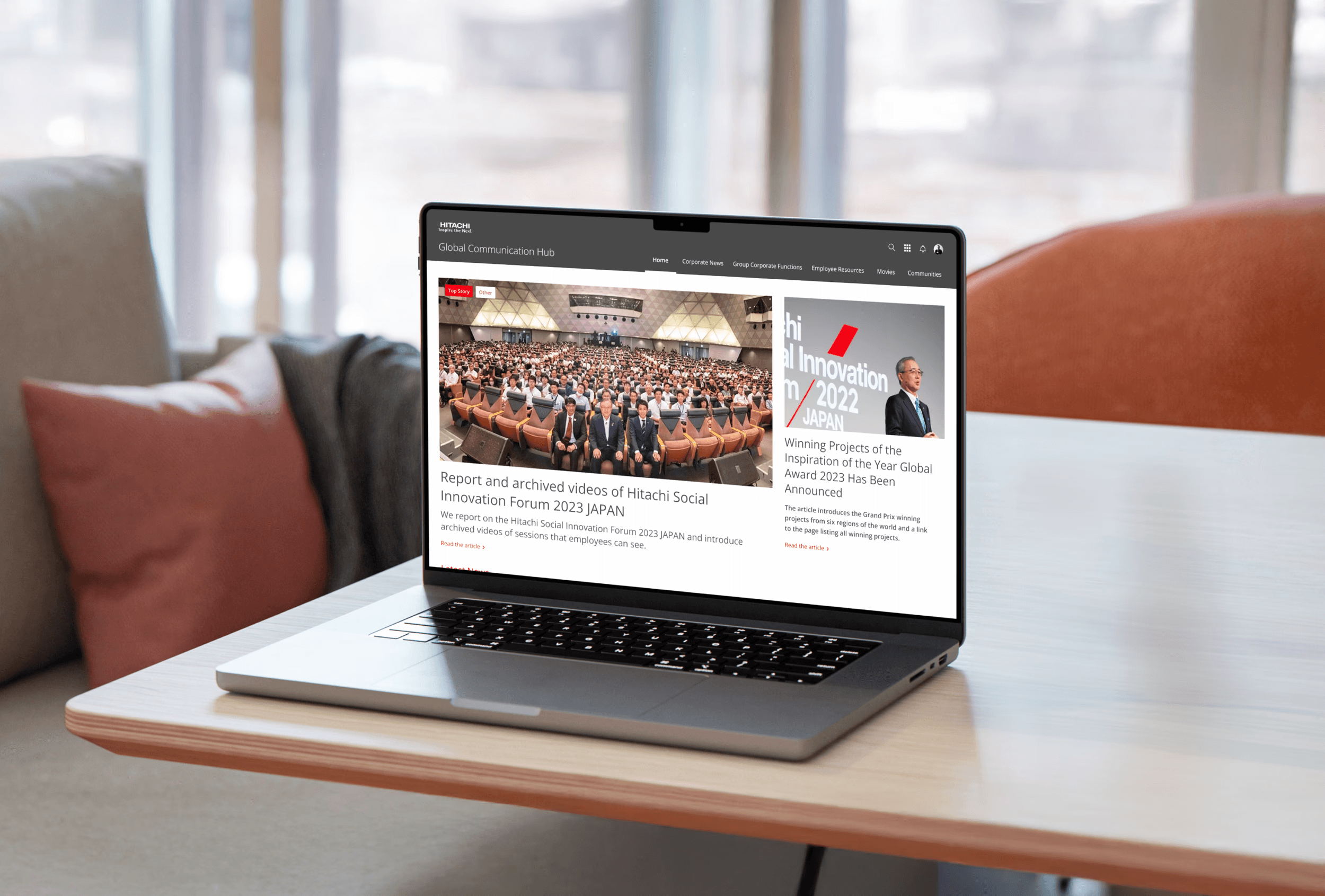Laptop displaying Hitachi's Global Communication Hub featuring company news articles and employee updates on modern desk