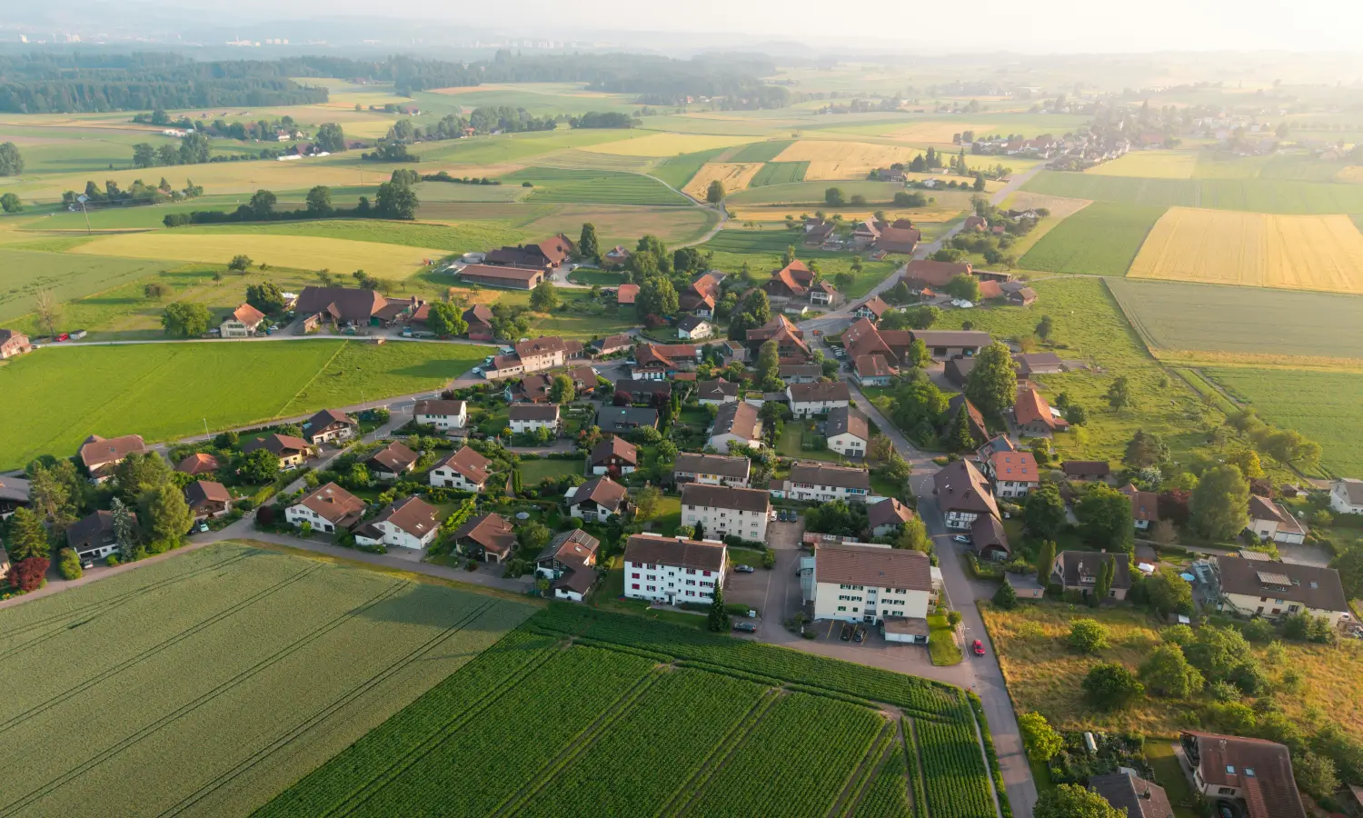 Luftaufnahme eines Dorfes mit umliegenden Feldern und Bauernbetrieben bei Sonnenuntergang.