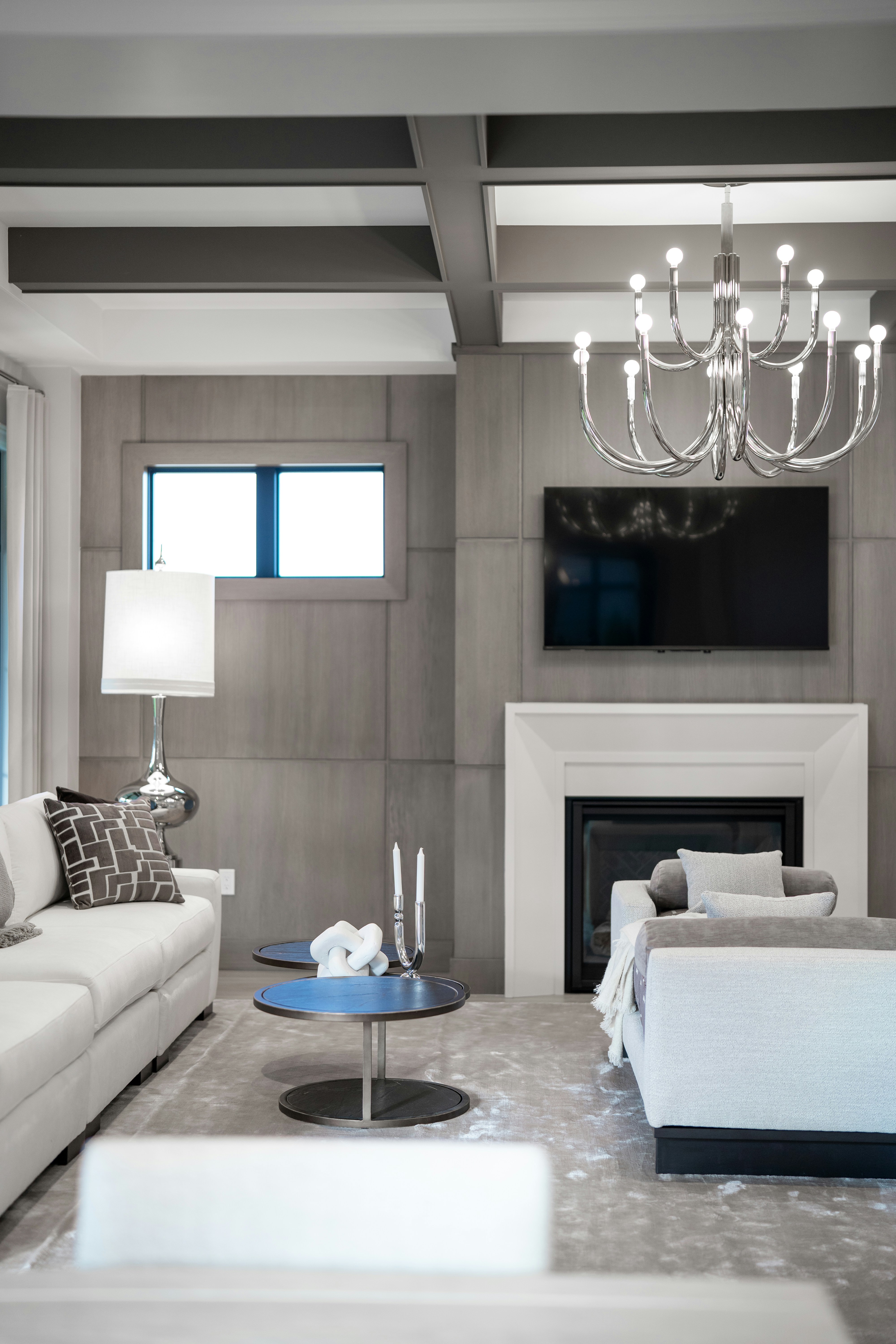 Modern living room with white sofas, fireplace, and chandelier.