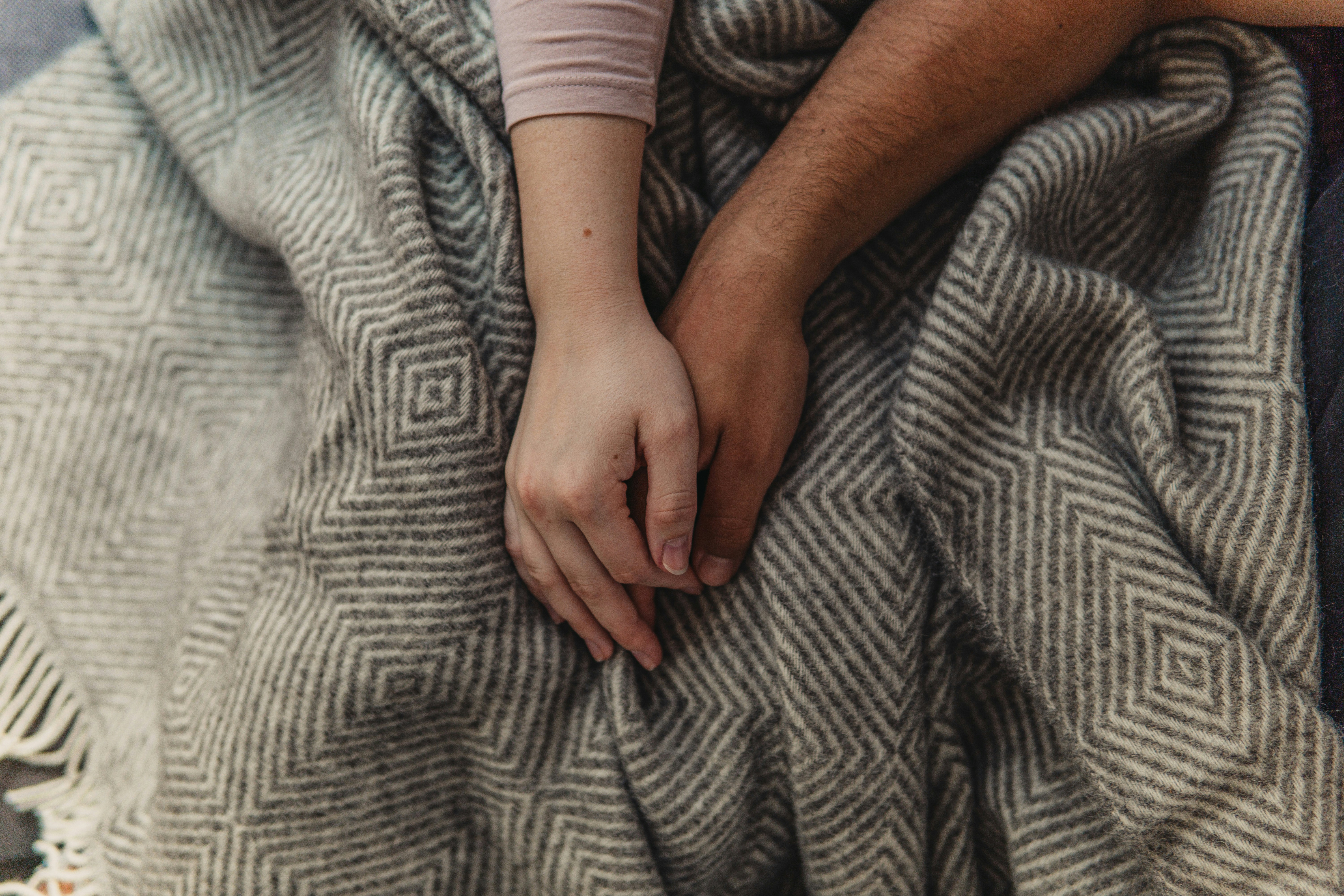 Two people holding hands under a blanket, representing emotional connection and the support counselling and therapy can offer after a breakup