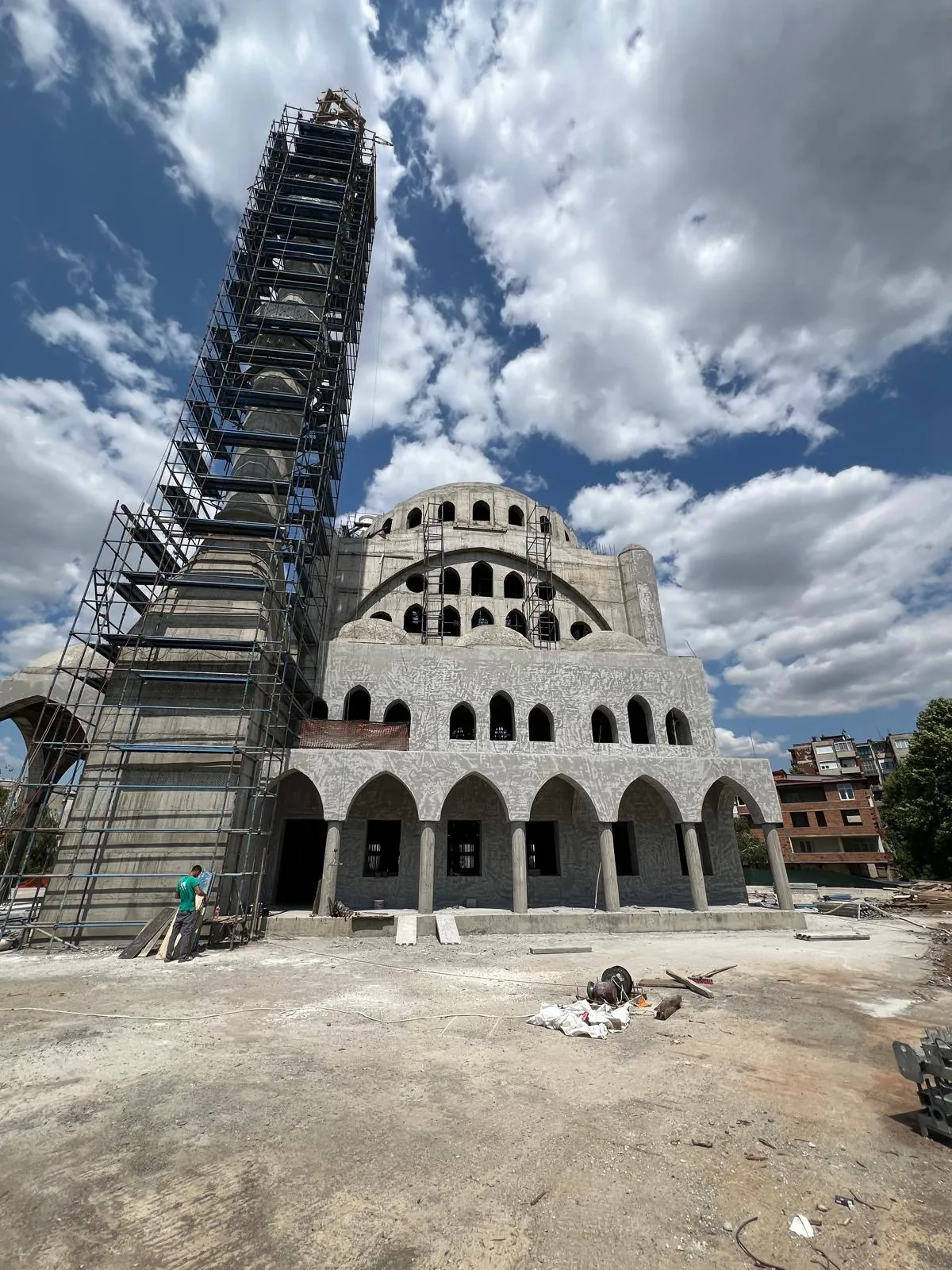 Large mosque in Skopje under construction with arched façades, scaffolding on both minarets, and surrounding urban context. Terraplan Partners handled project supervision.