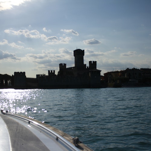 Silhouette of a castle with towers by the water, viewed from a boat, under a partly cloudy sky.