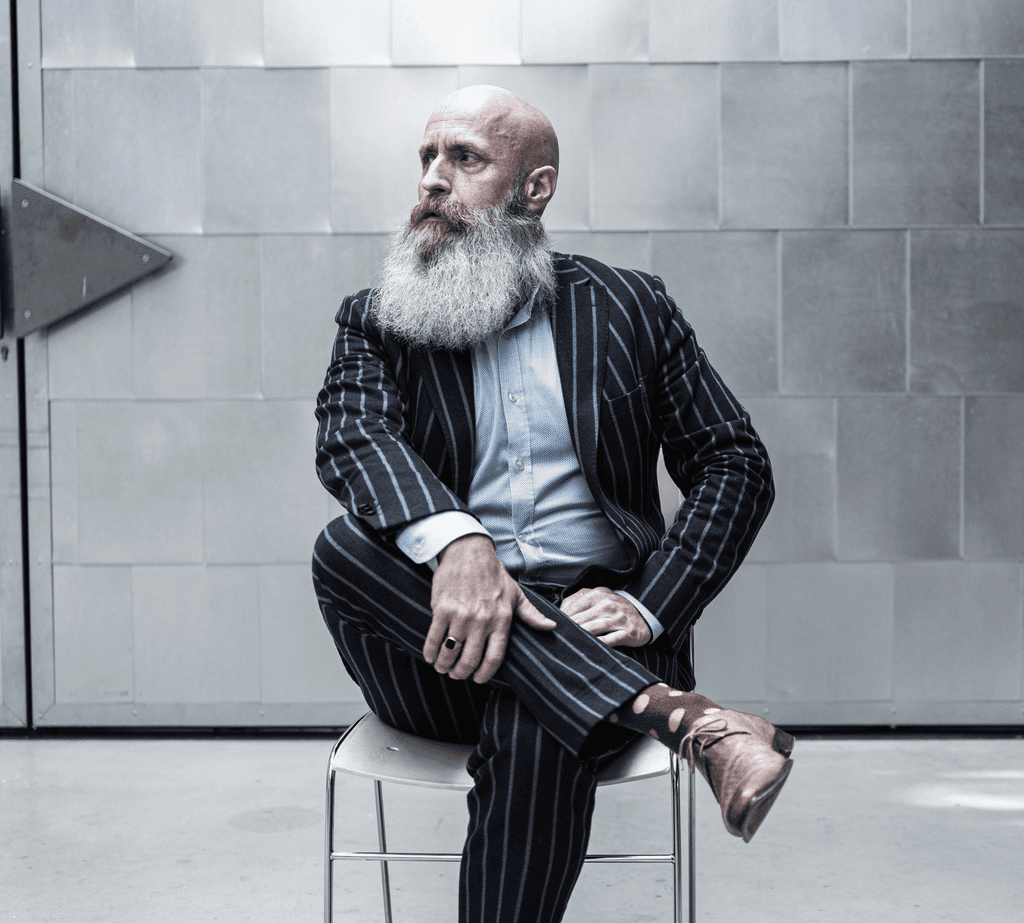 Foto van Bas Stronks, die marketeer met die baard, in streepjespak, roze schoenen, in industriele setting.