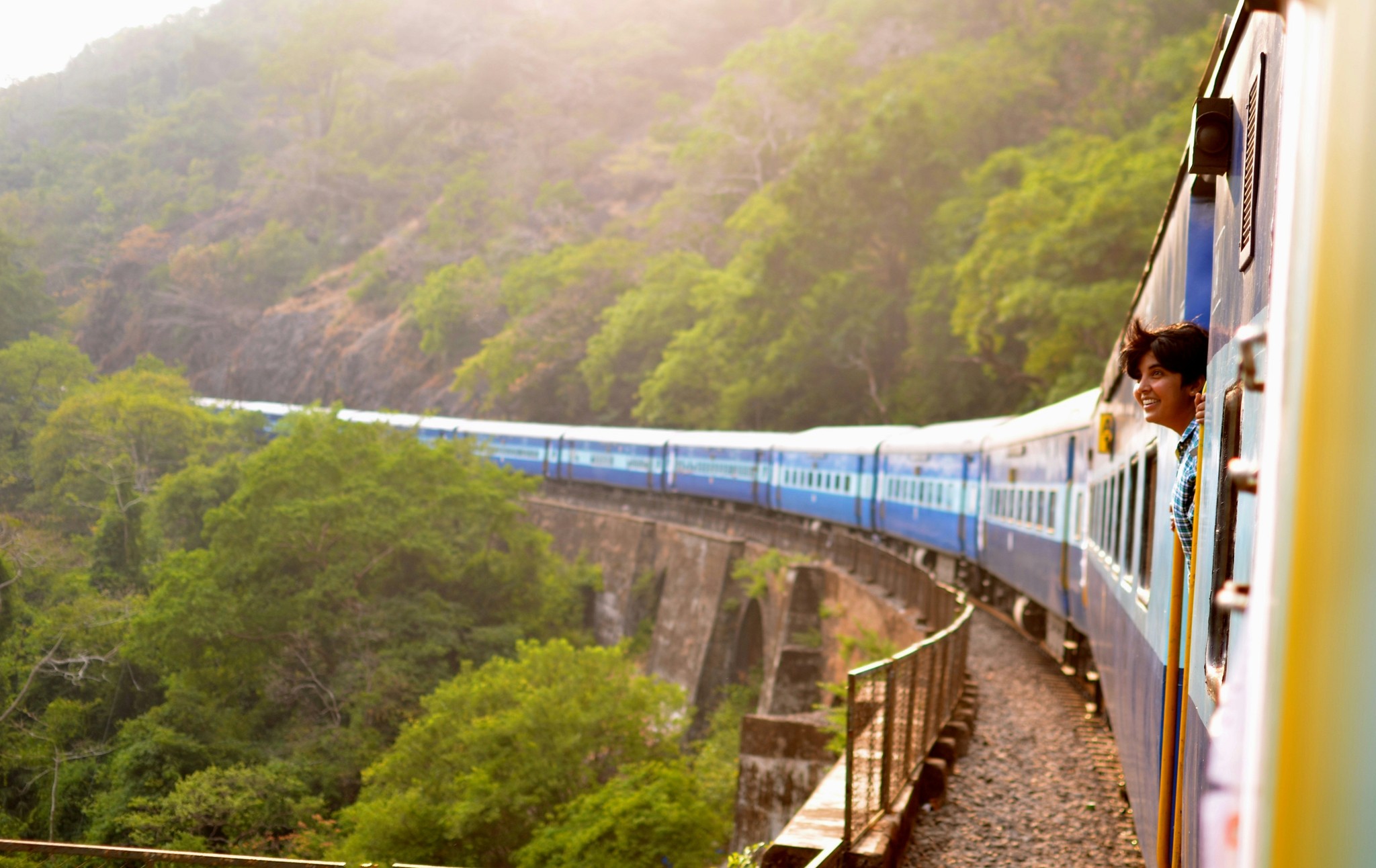 A woman looks out from a train as it rounds a bend along a forested ridge