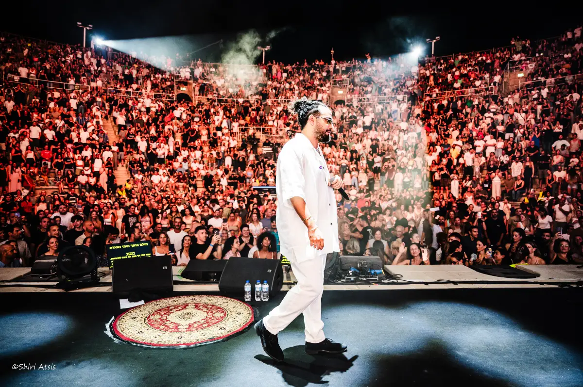 בניה בראבי צועד על הבמה בקיסריה אל מול קהל מעריצים, צילום הופעות אומנותי של שירי עציץ - Shiriz.