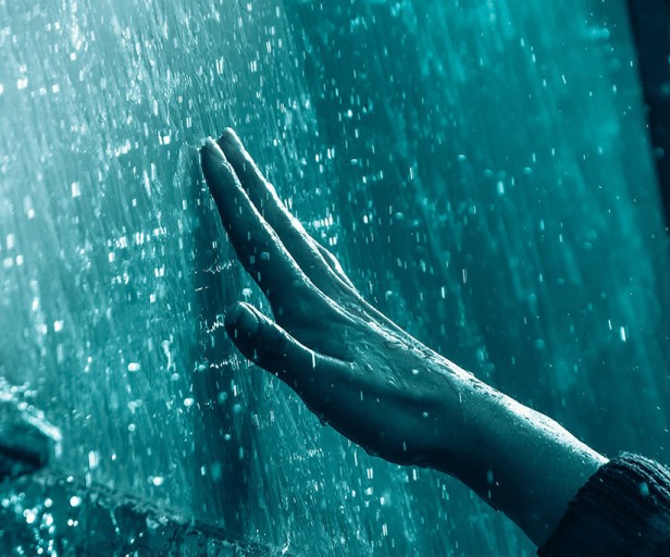 A hand reaches out to a wet glass surface, with water droplets and a blue-tinted background.