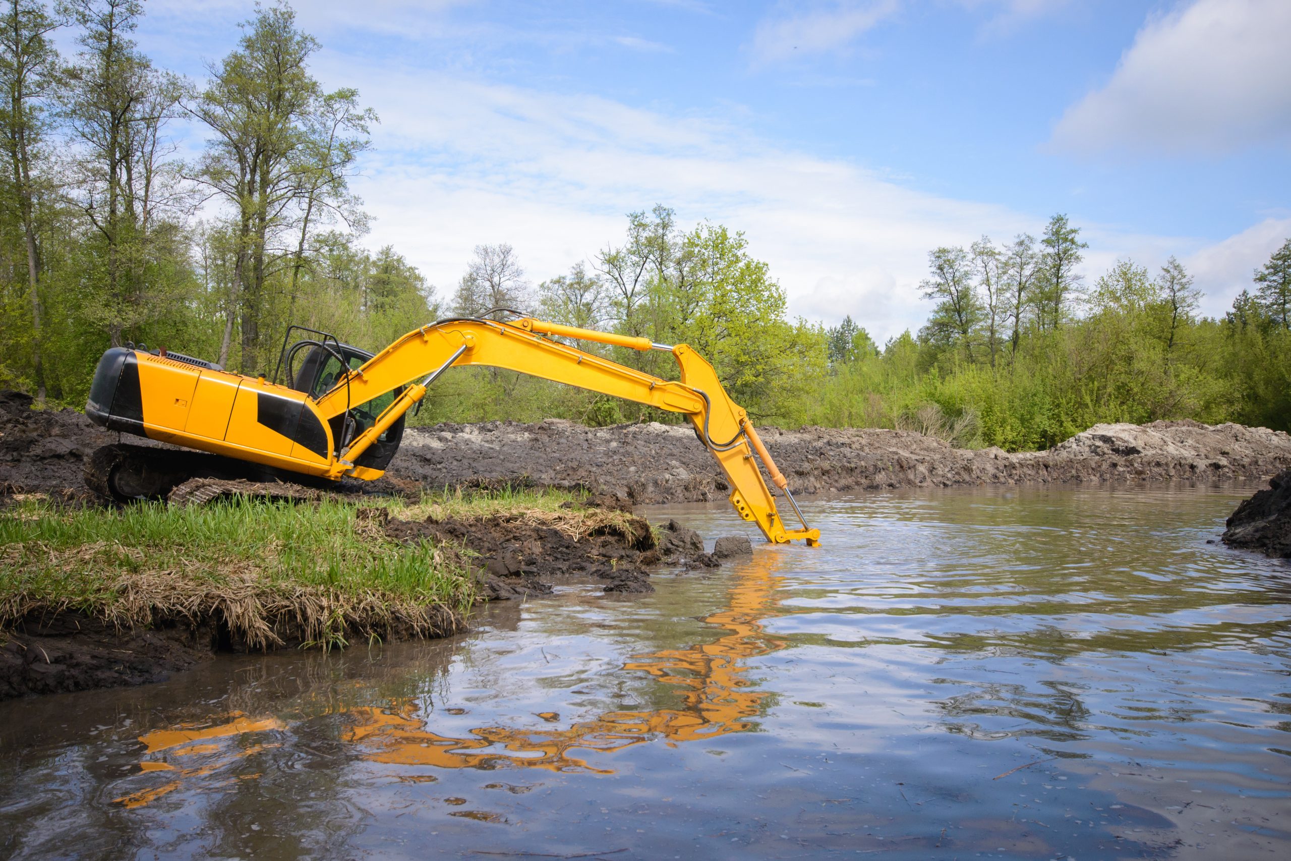 Excavator removing sediment during a pond dredging project to restore depth and shoreline stability.