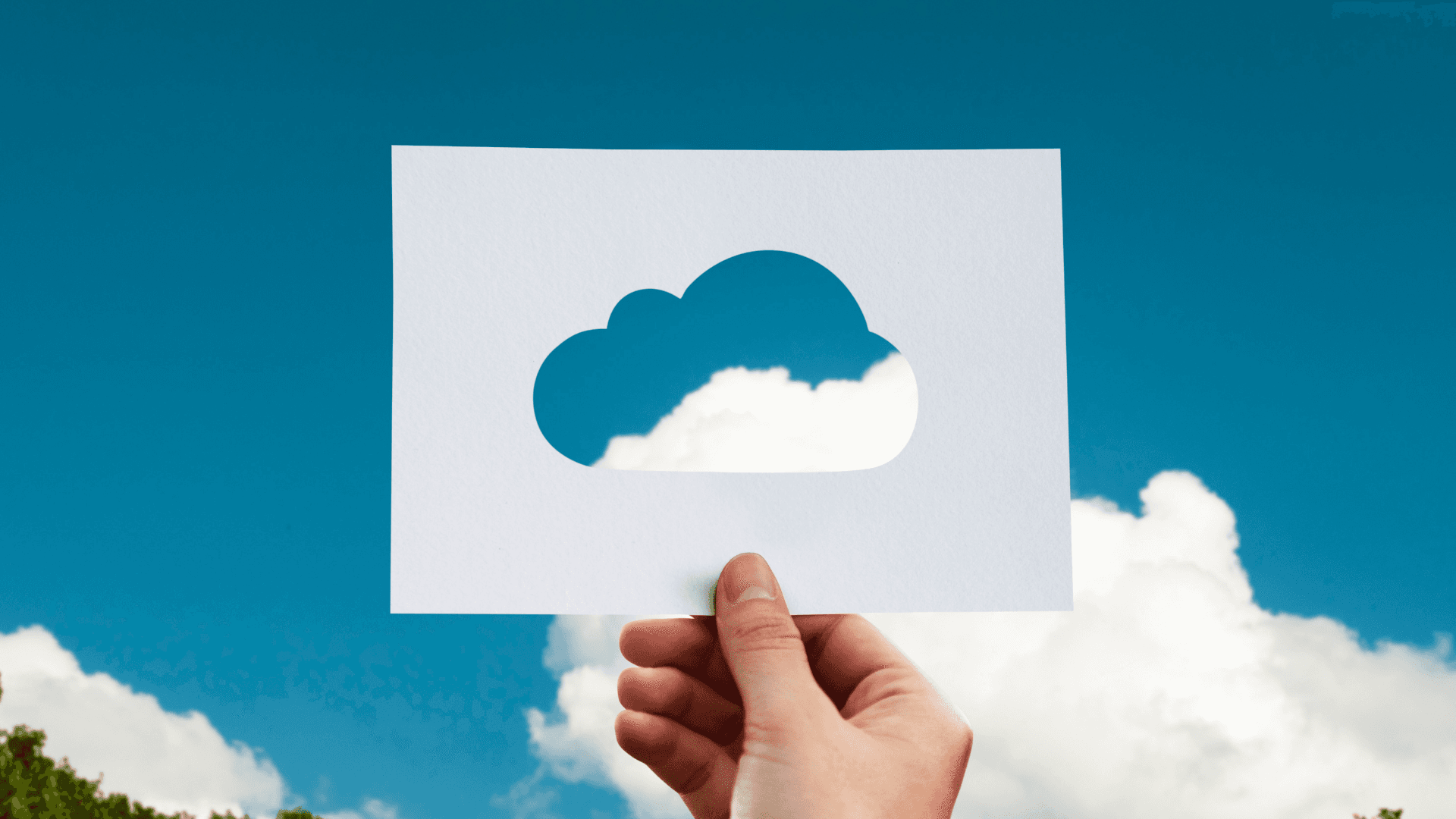 A piece of paper with a cloud cut out being held up to a blue sky with white clouds