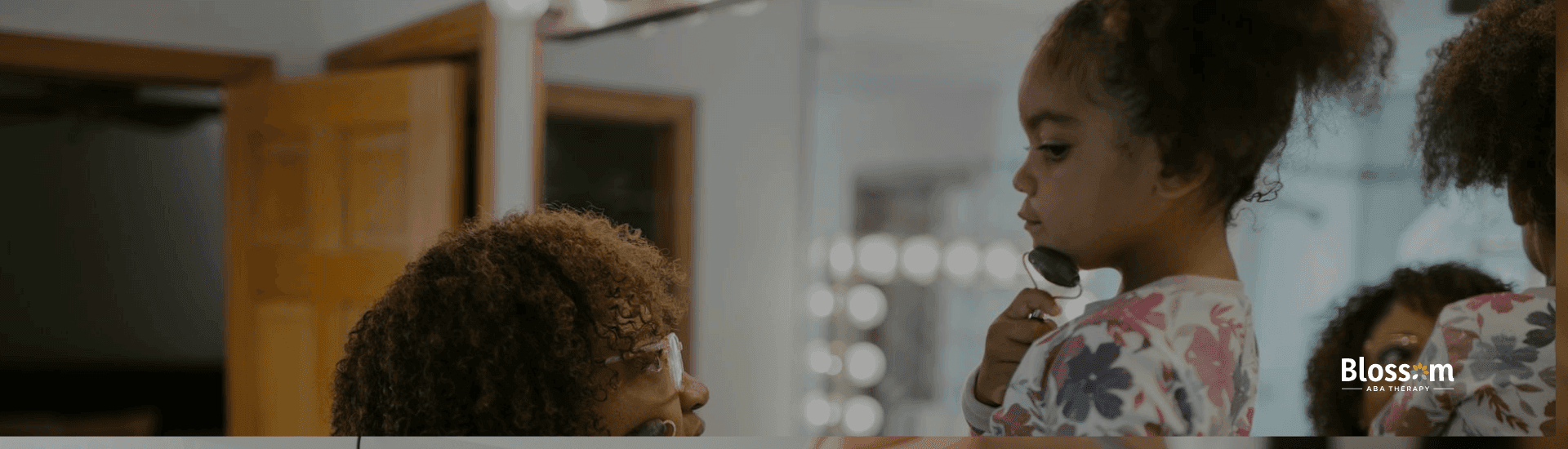 Female ABA therapist is applying a skincare roller on her patient autistic young girl face in a bathroom.