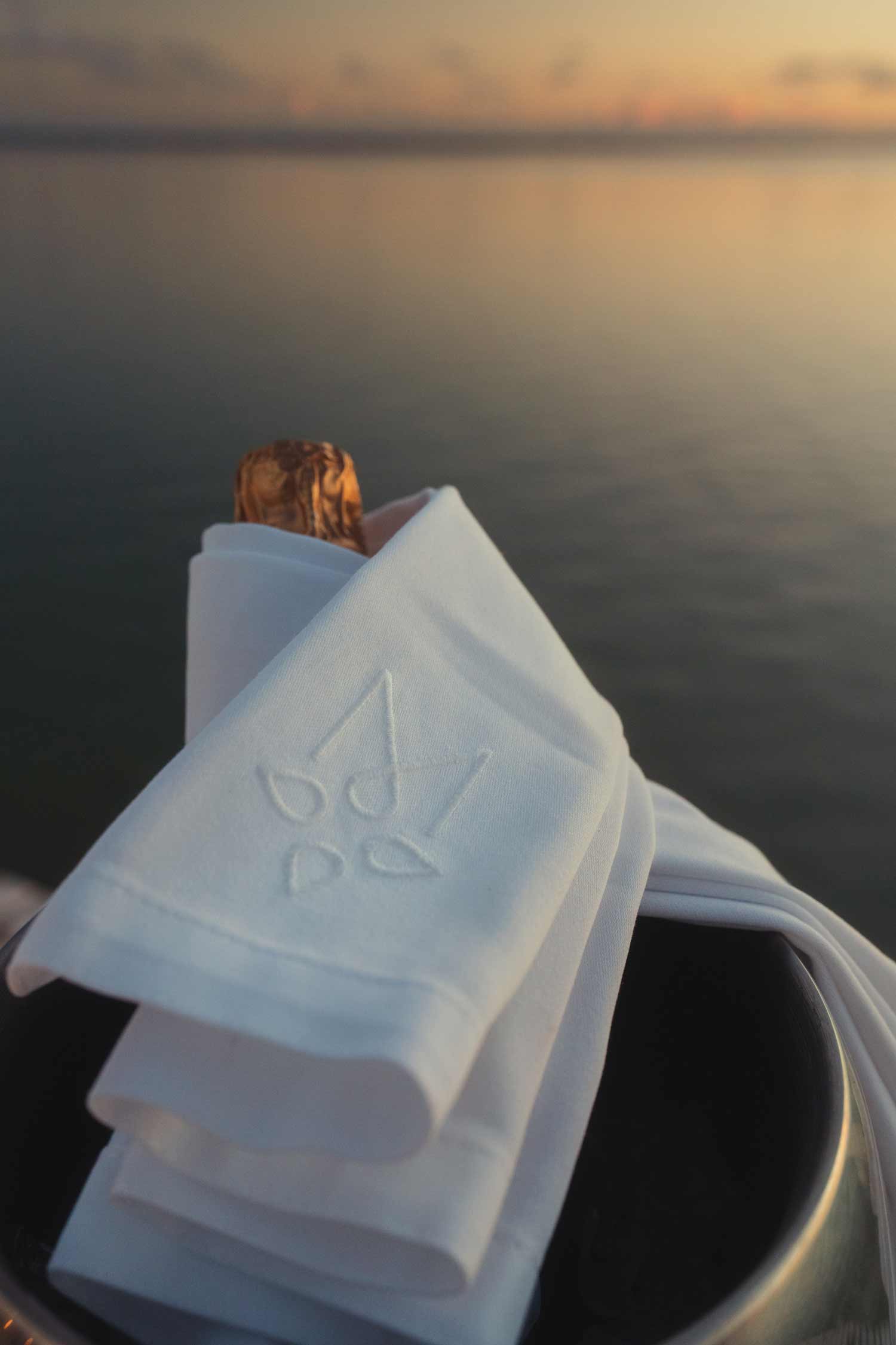 Champagne bottle draped in cloth by serene lake, maradiva client logo on cloth