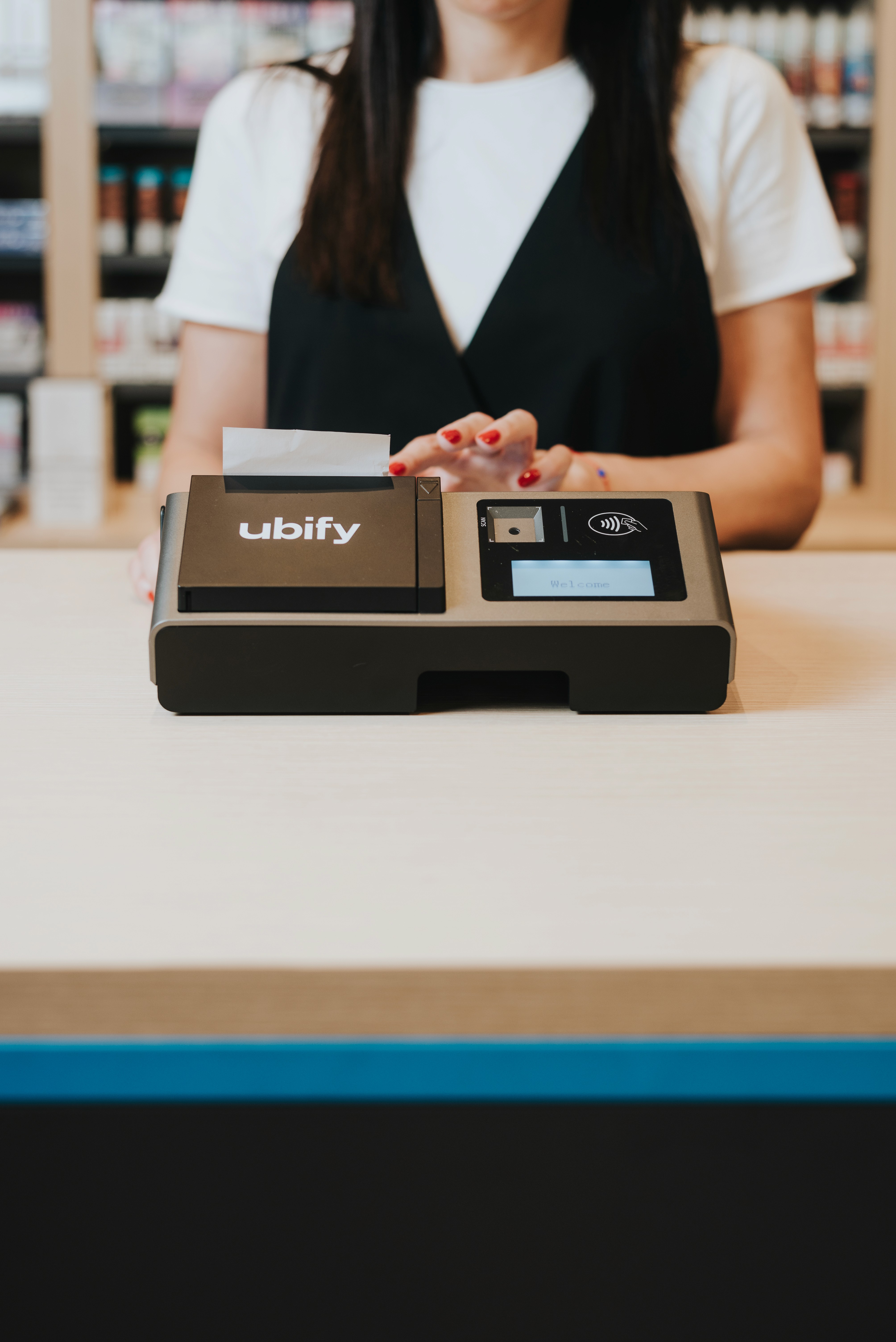 Commerciante dietro al bancone con la Cassa Ubify in primo piano, pronta per l’uso con scontrino stampato e display attivo.