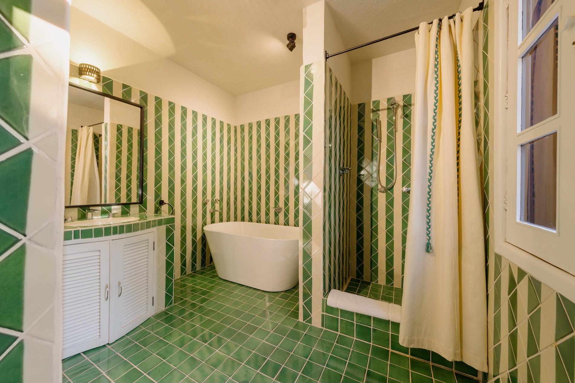 La Residencia bathroom with green geometric tile, freestanding tub, and walk-in shower