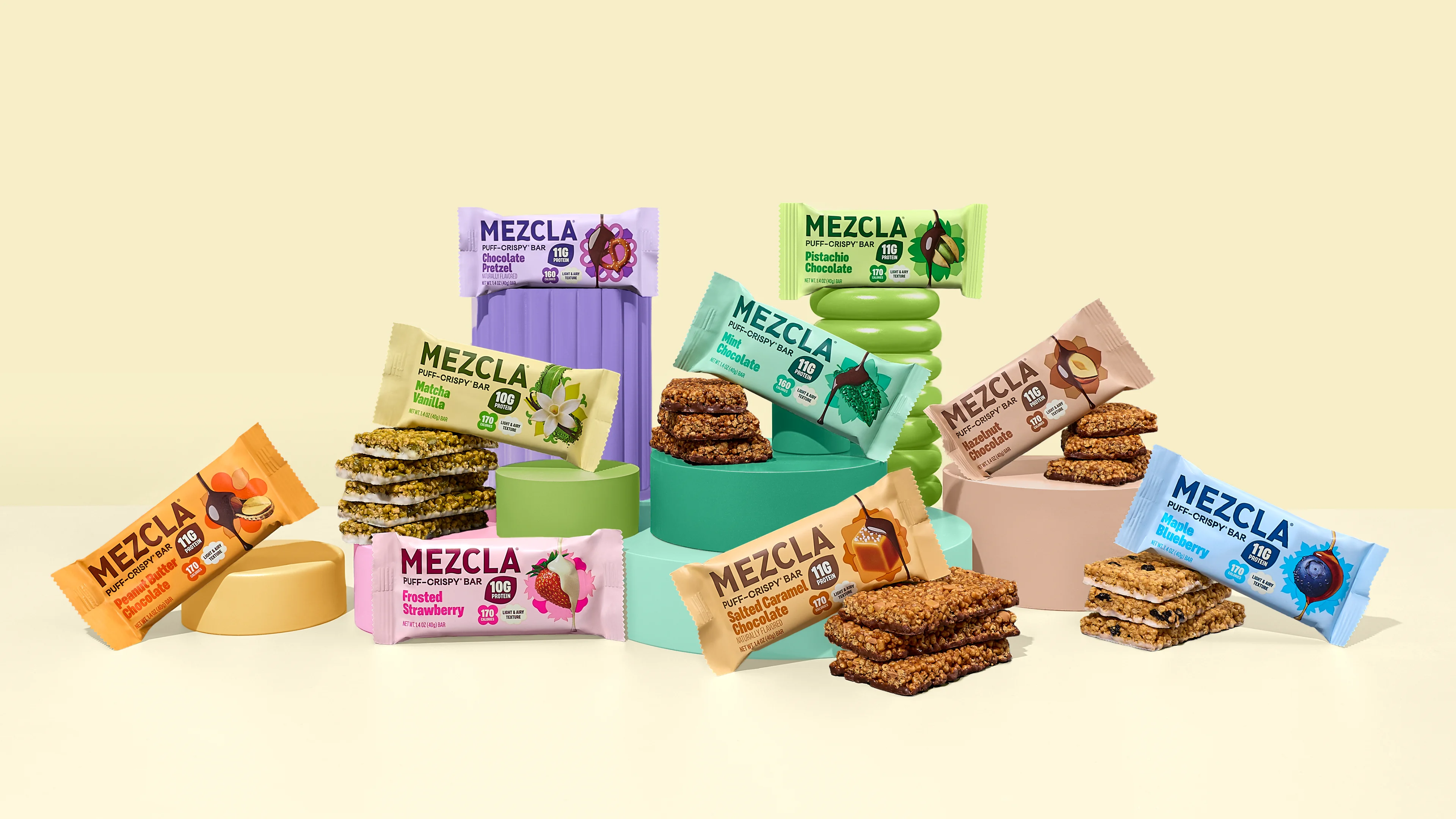 Mezcla full range of nine protein bar flavors arranged on pastel plinths against a cream background