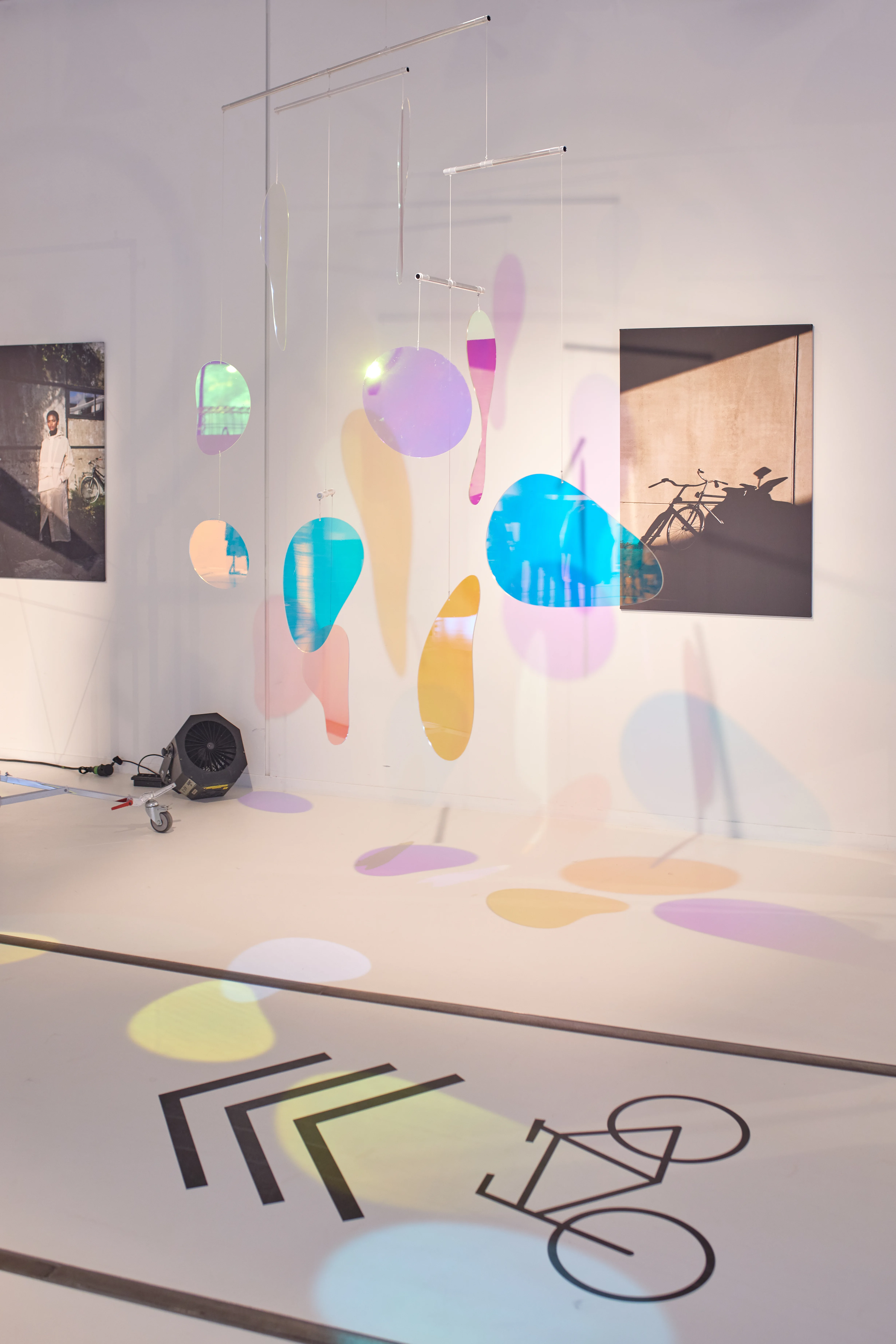 Mobile of colorful iridescent acrylic shapes casting rainbow reflections in the white AGU exhibition space.