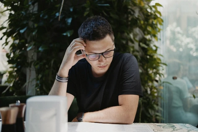Man sitting indoors and looking down in concentration beside leafy plants