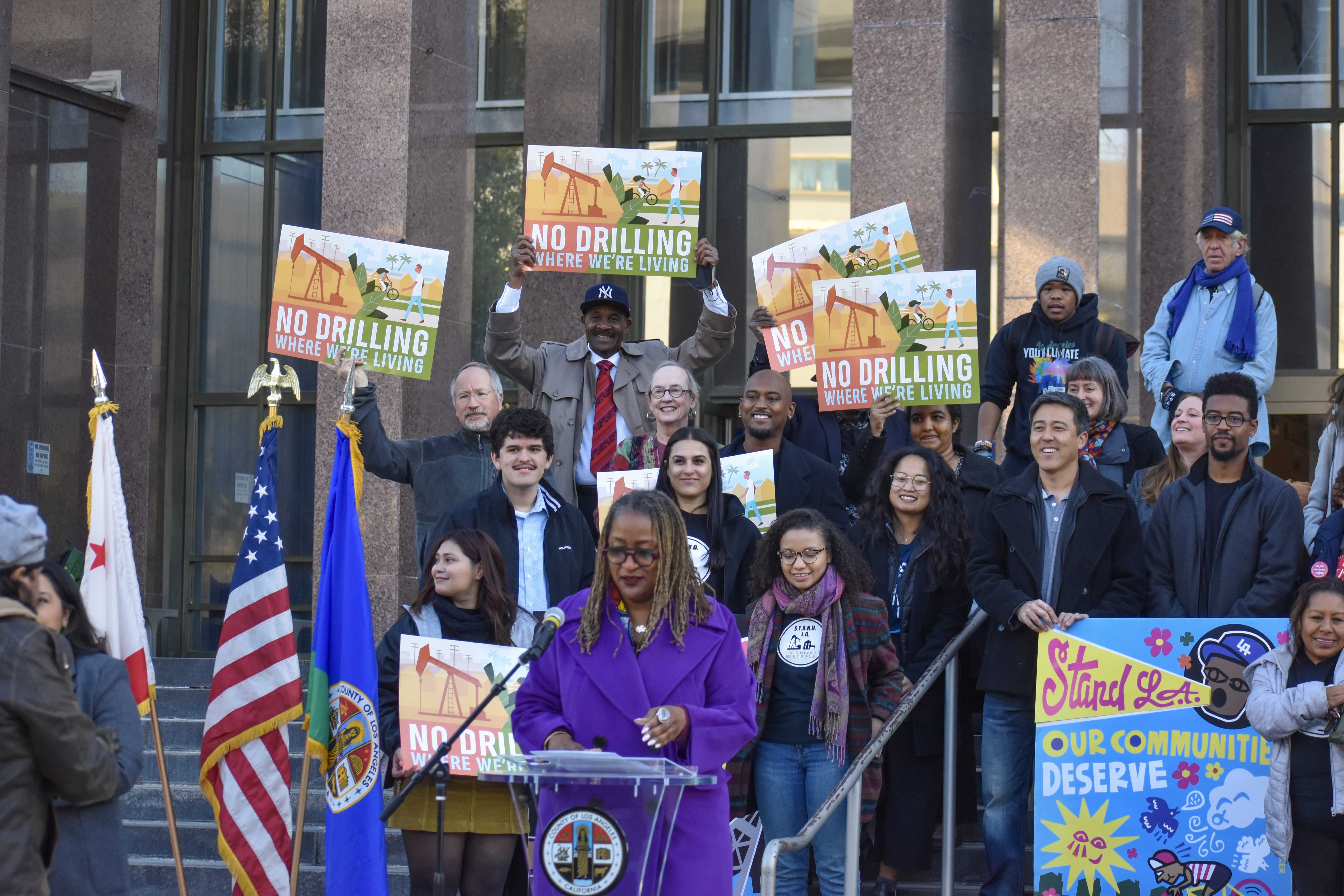 A rally against Big Oil with a woman speaking in front of a crowd behind her.