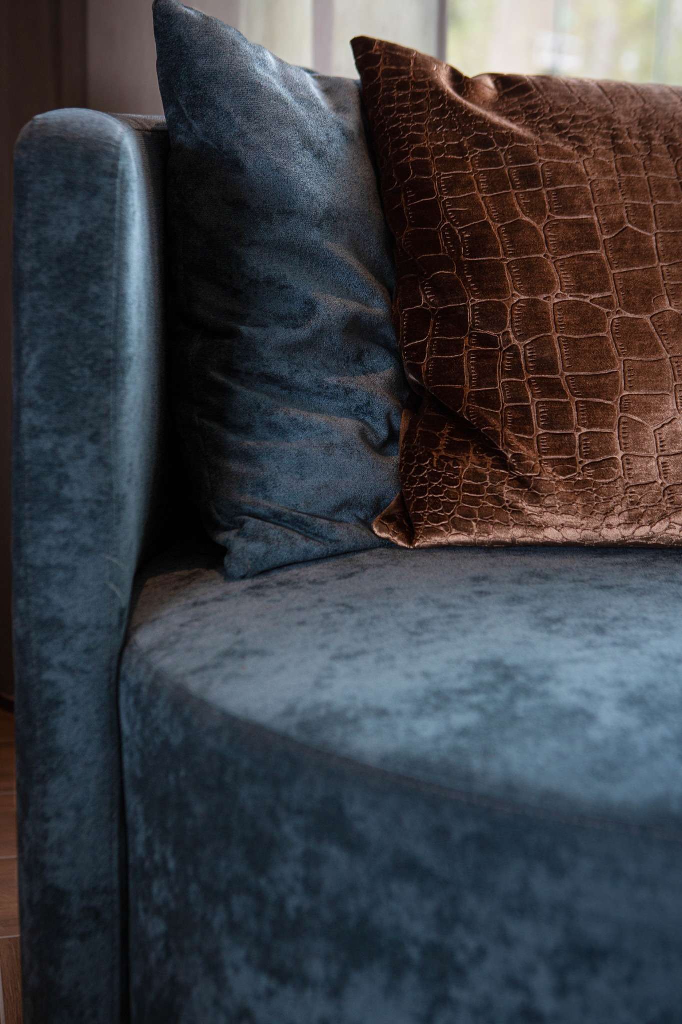 Detail van een blauwe fauteuil met velvet sierkussens in warme tinten.