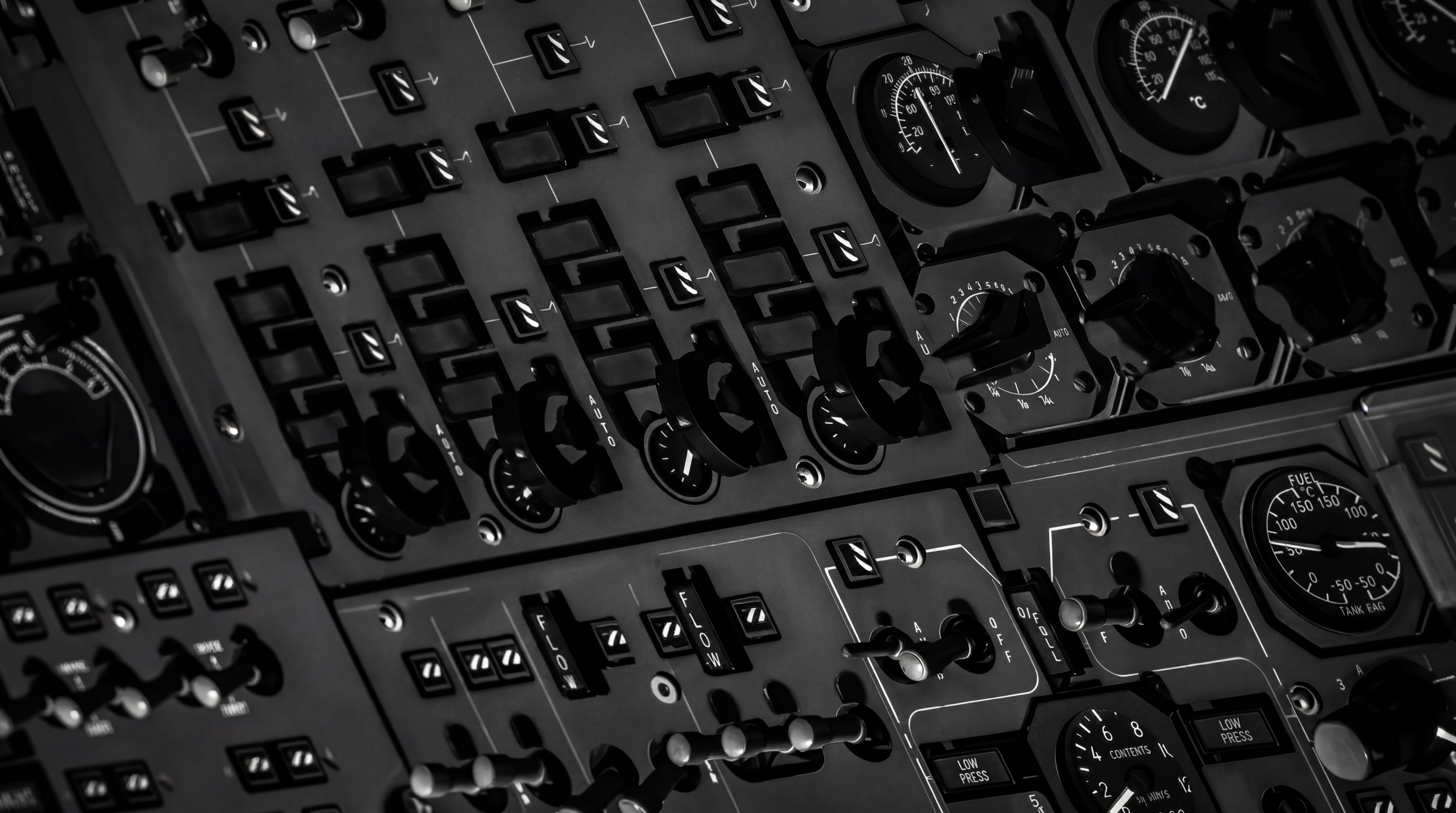Black and white close-up of an aircraft control panel with switches, dials, and levers in a structured layout.