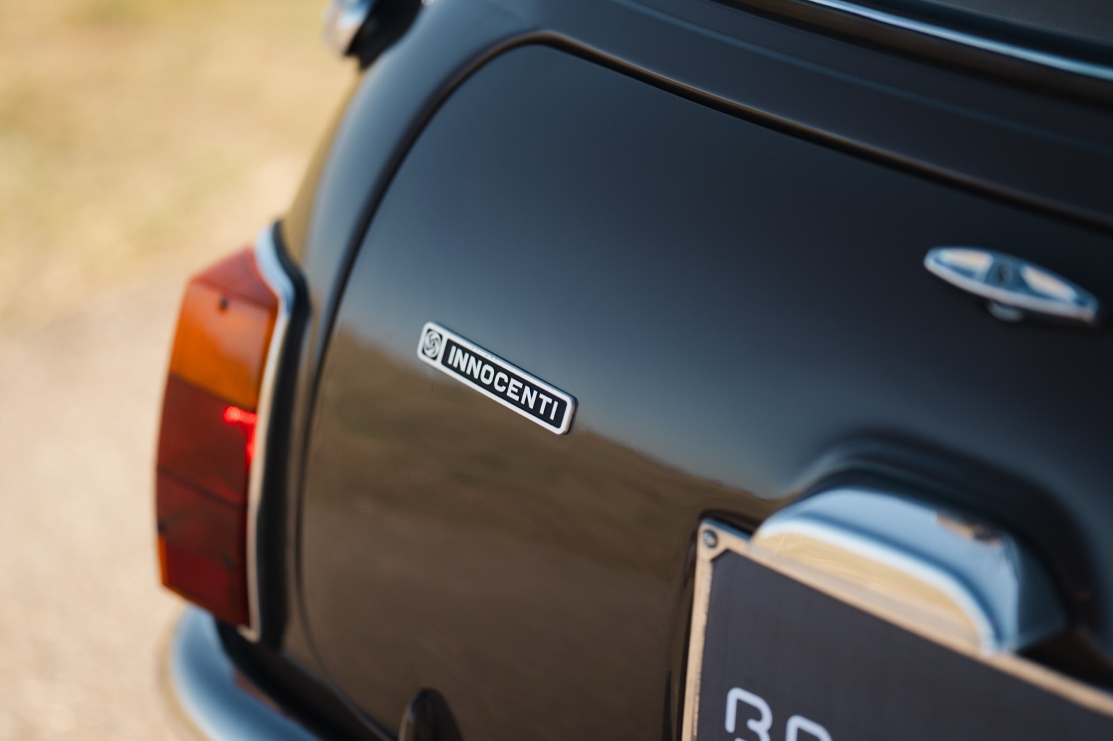 A close-up of the rear end of a classic car, featuring a taillight and a shiny surface reflecting light.