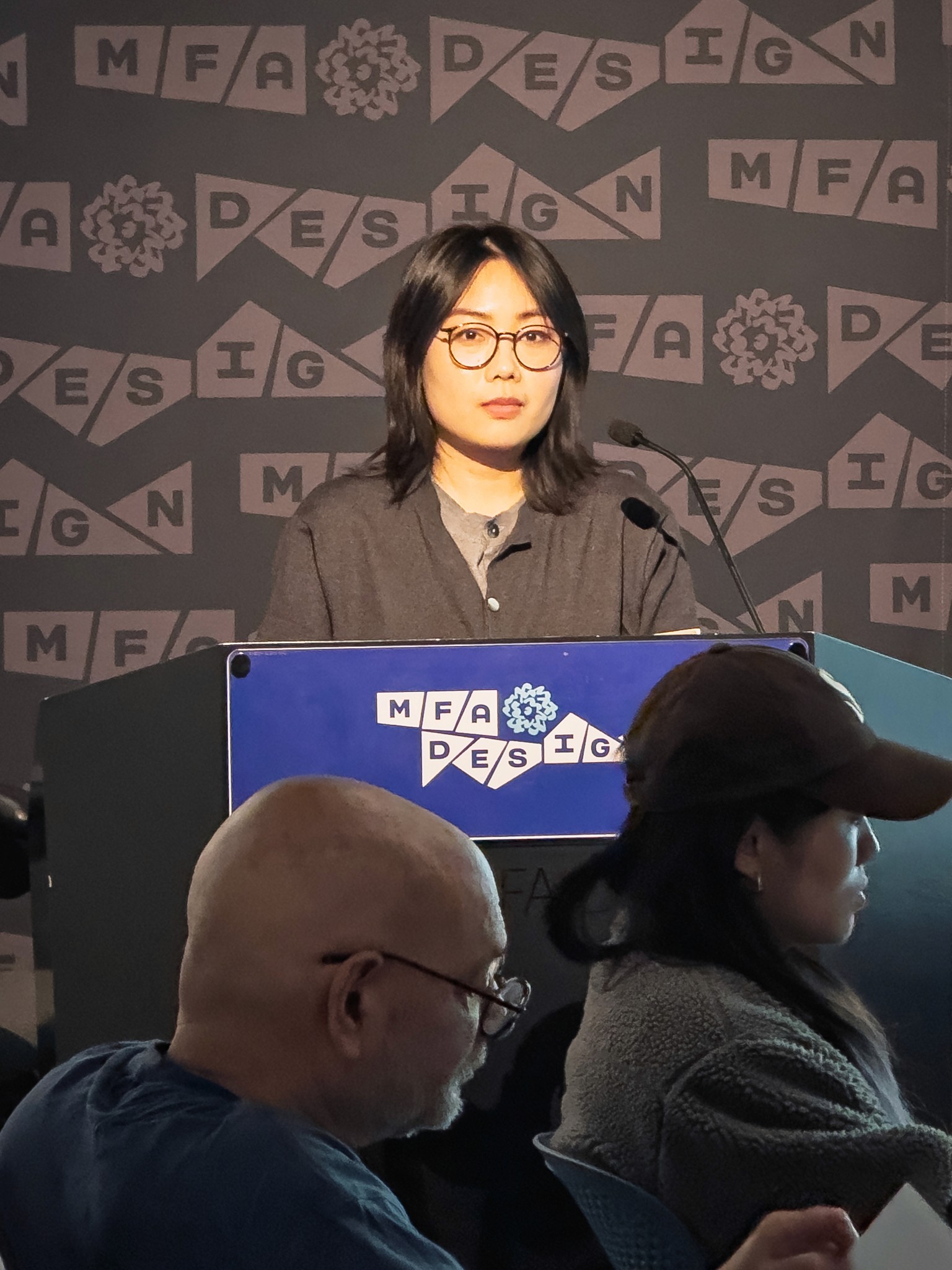 Woman at a podium with microphone, delivering a slide presentation