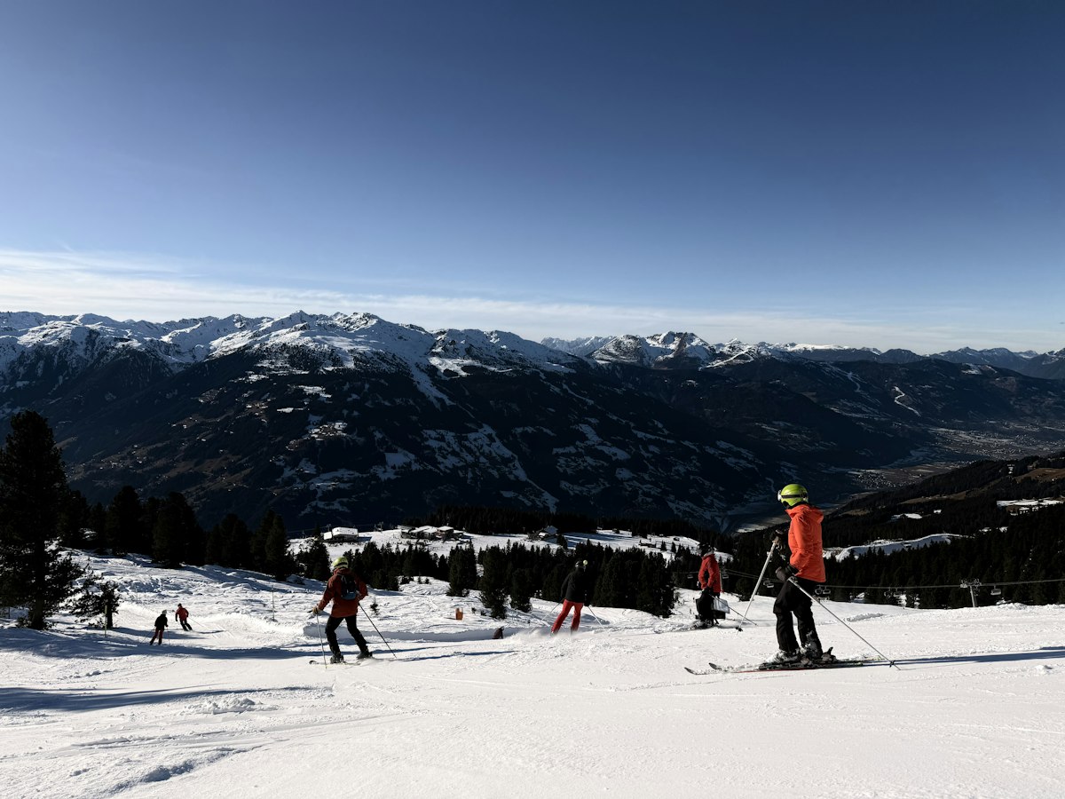Skiers spread across a wide open run with a snow covered mountain range on the horizon