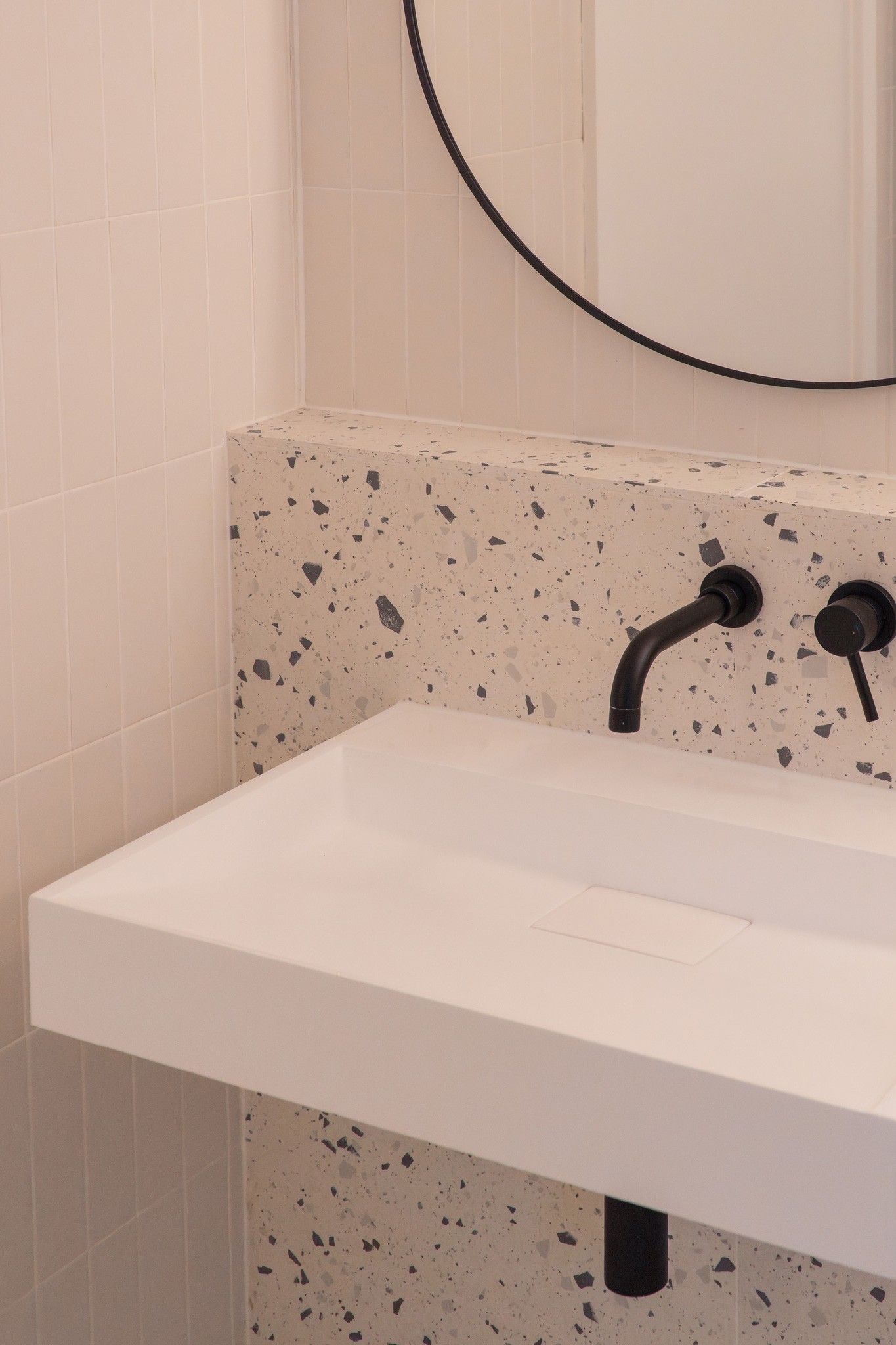 Close-up detail of terrazzo splashback tiles with white countertop sink and black wall-mounted tap, London architect-designed bathroom