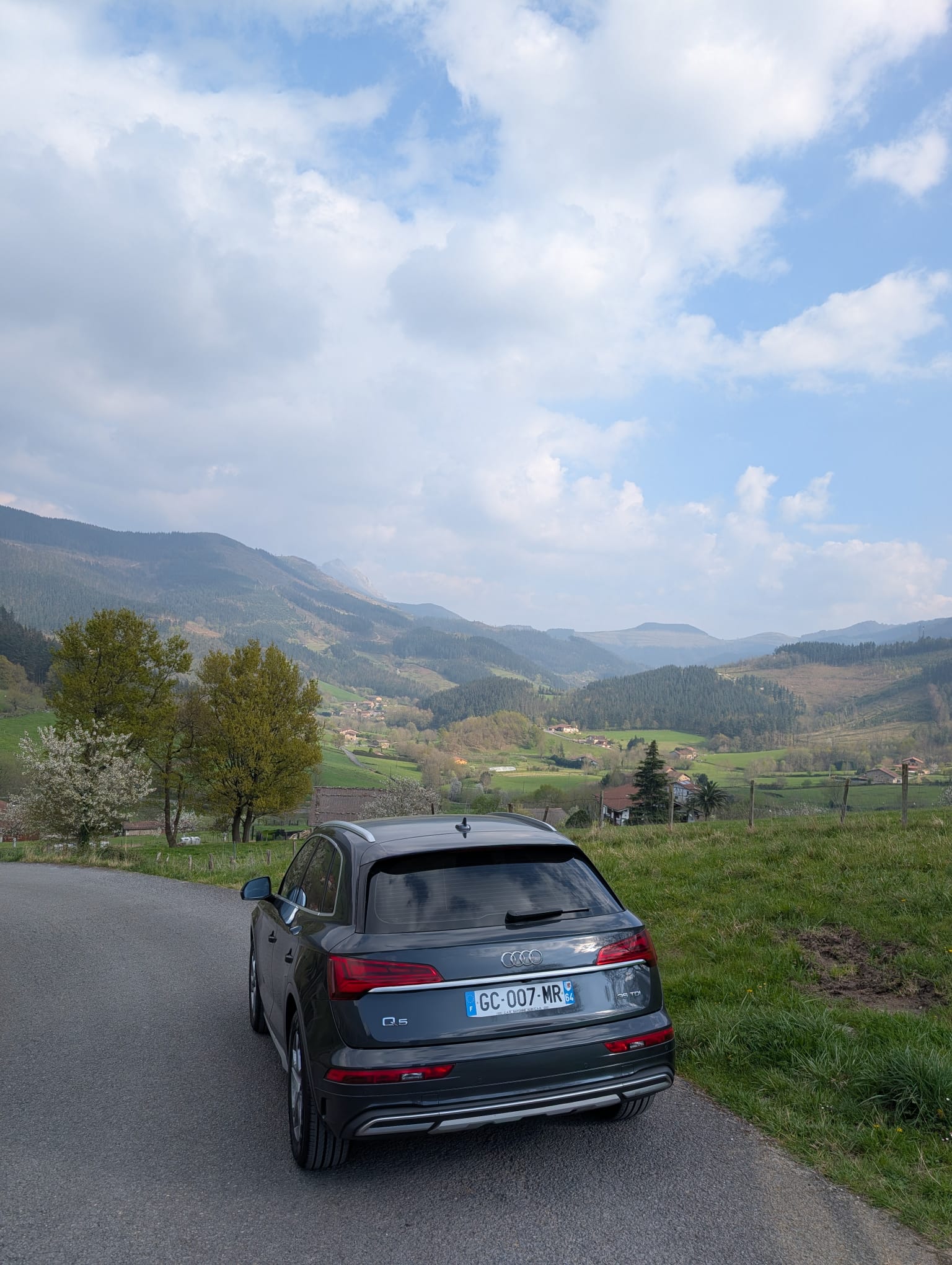 A person walks along a seaside pathway, gesturing with one hand, wearing a jacket and casual shoes.
