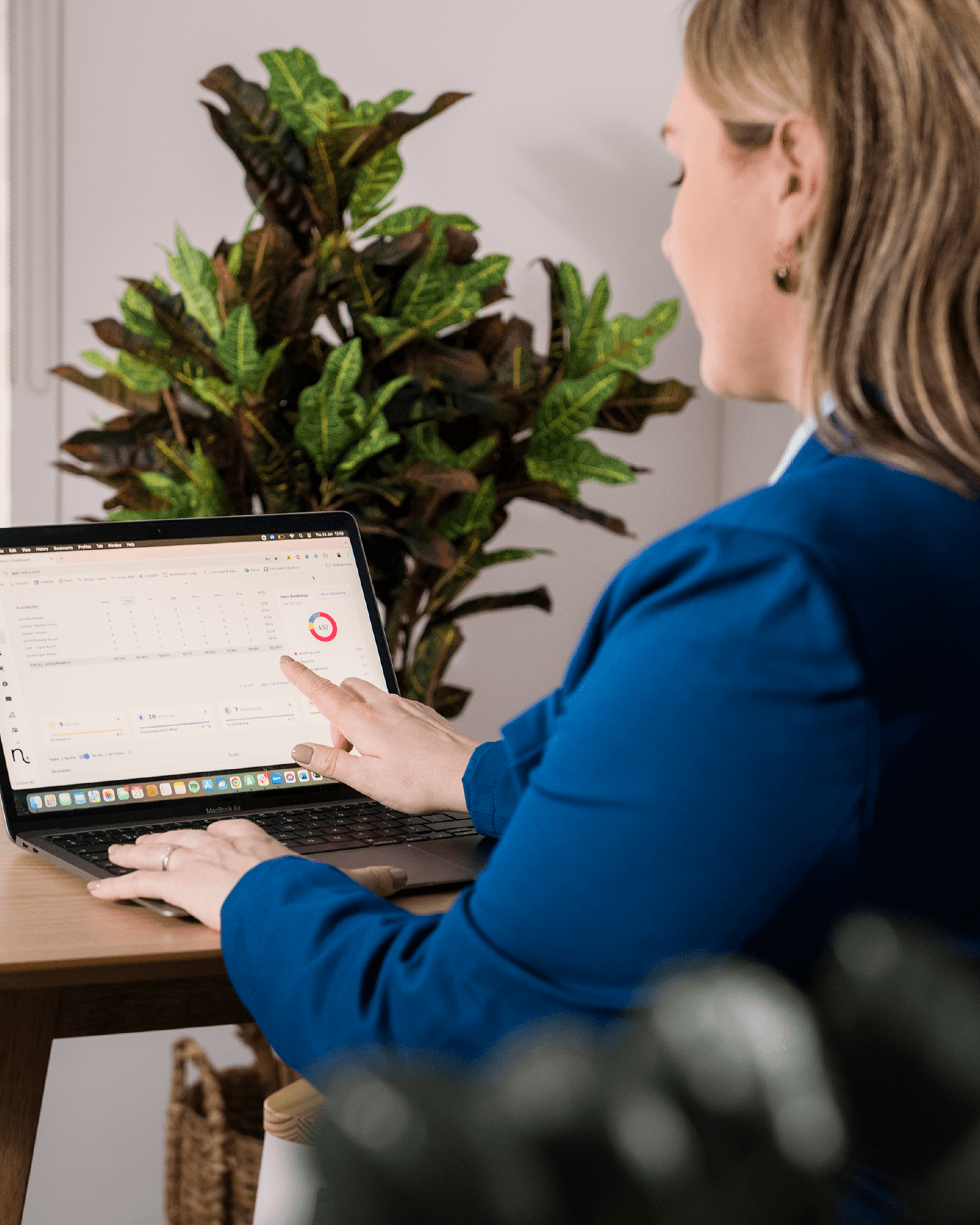 A person in a blue shirt sits at a desk, using a tablet, with a plant visible in the background.