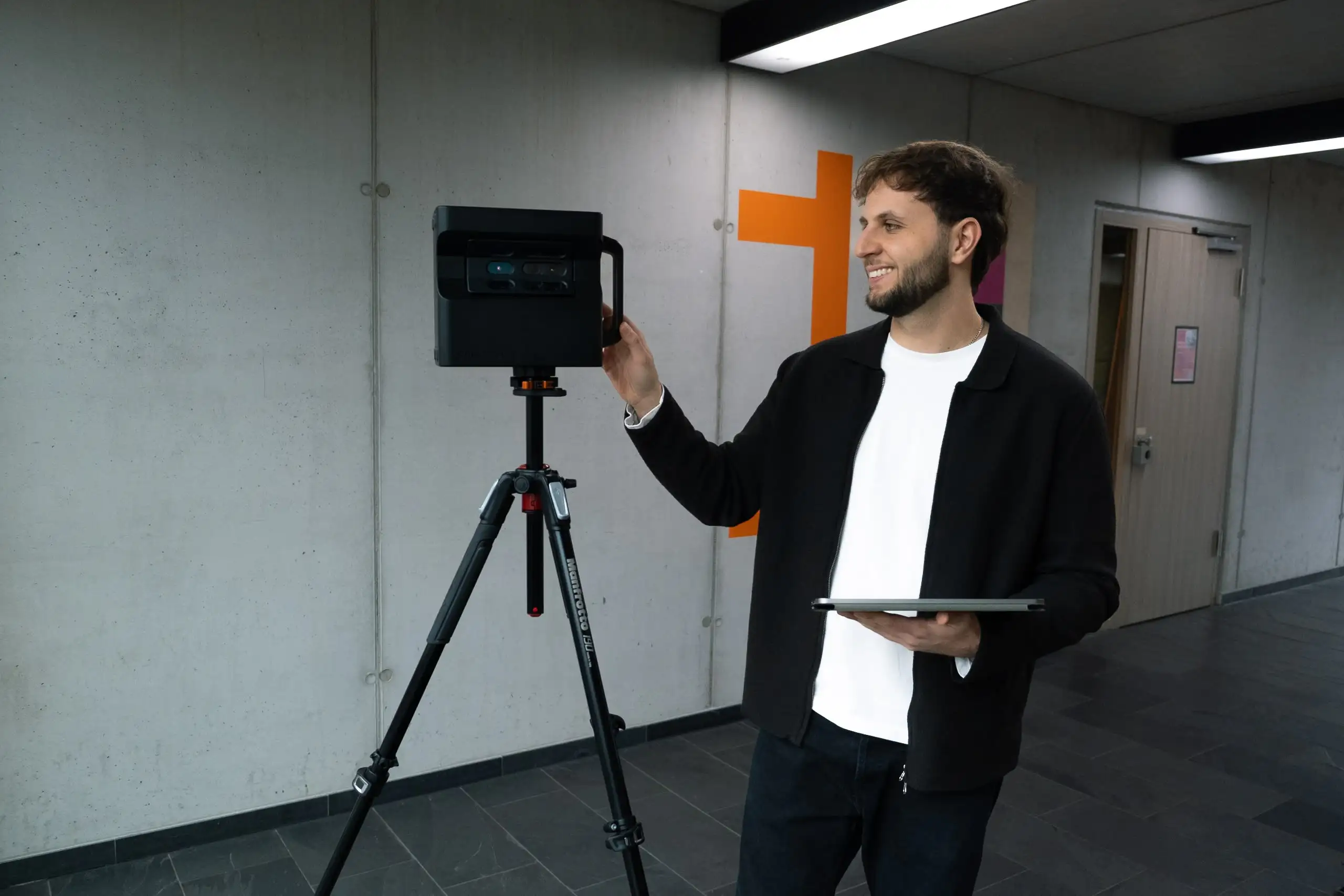 Person standing next to a tripod-mounted camera, adjusting settings in a well-lit indoor setting.