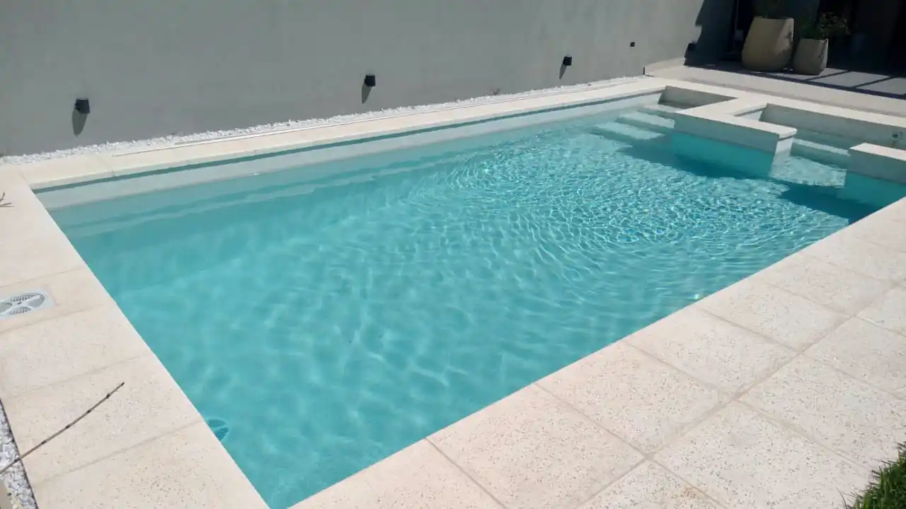 Pileta de hormigón armado con revestimiento continuo Aquavations en tono claro, destacando escalones internos y un sector de descanso en el agua.