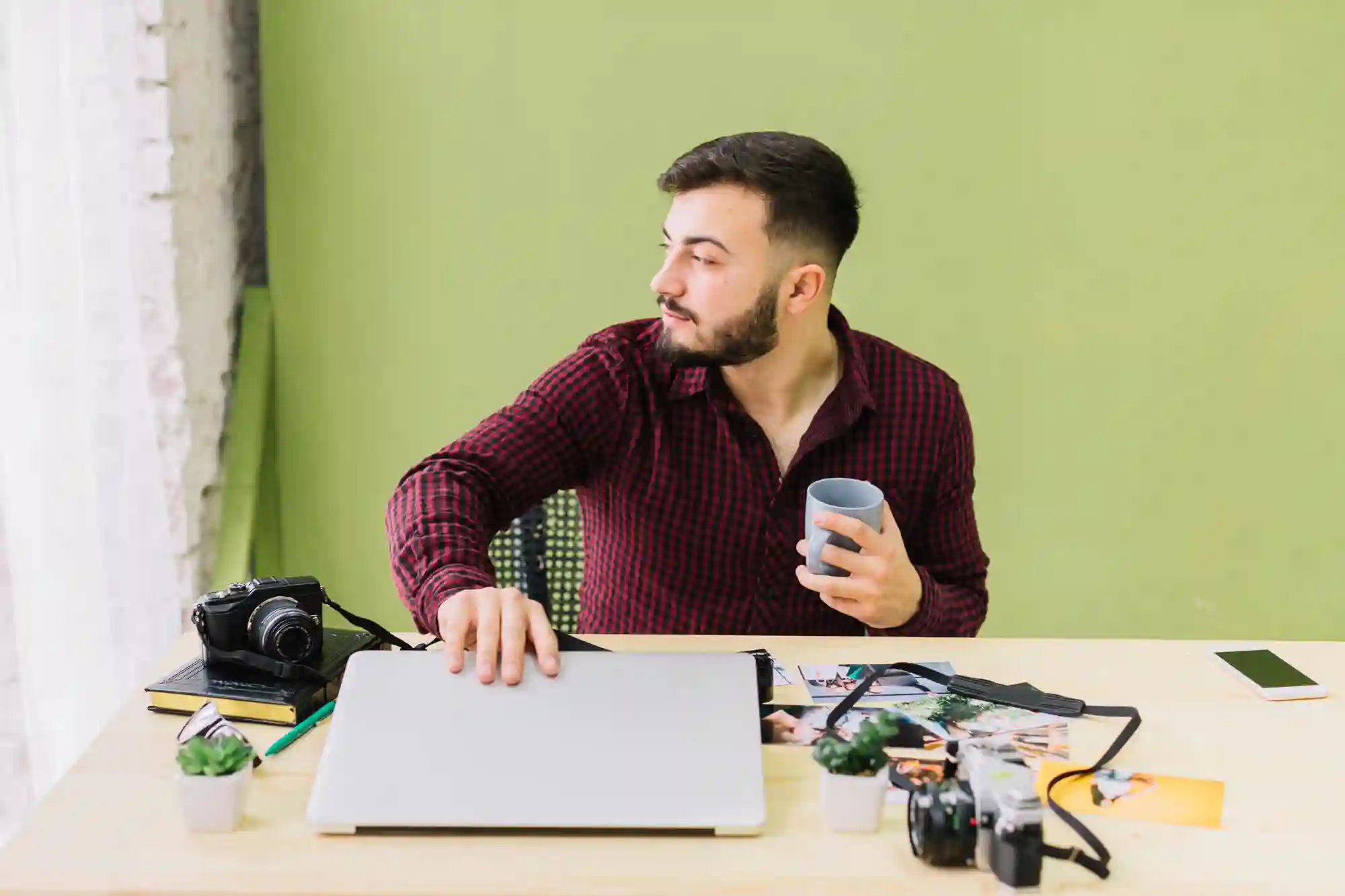 Man with a beard sitting at a cluttered desk looking away from the camera.