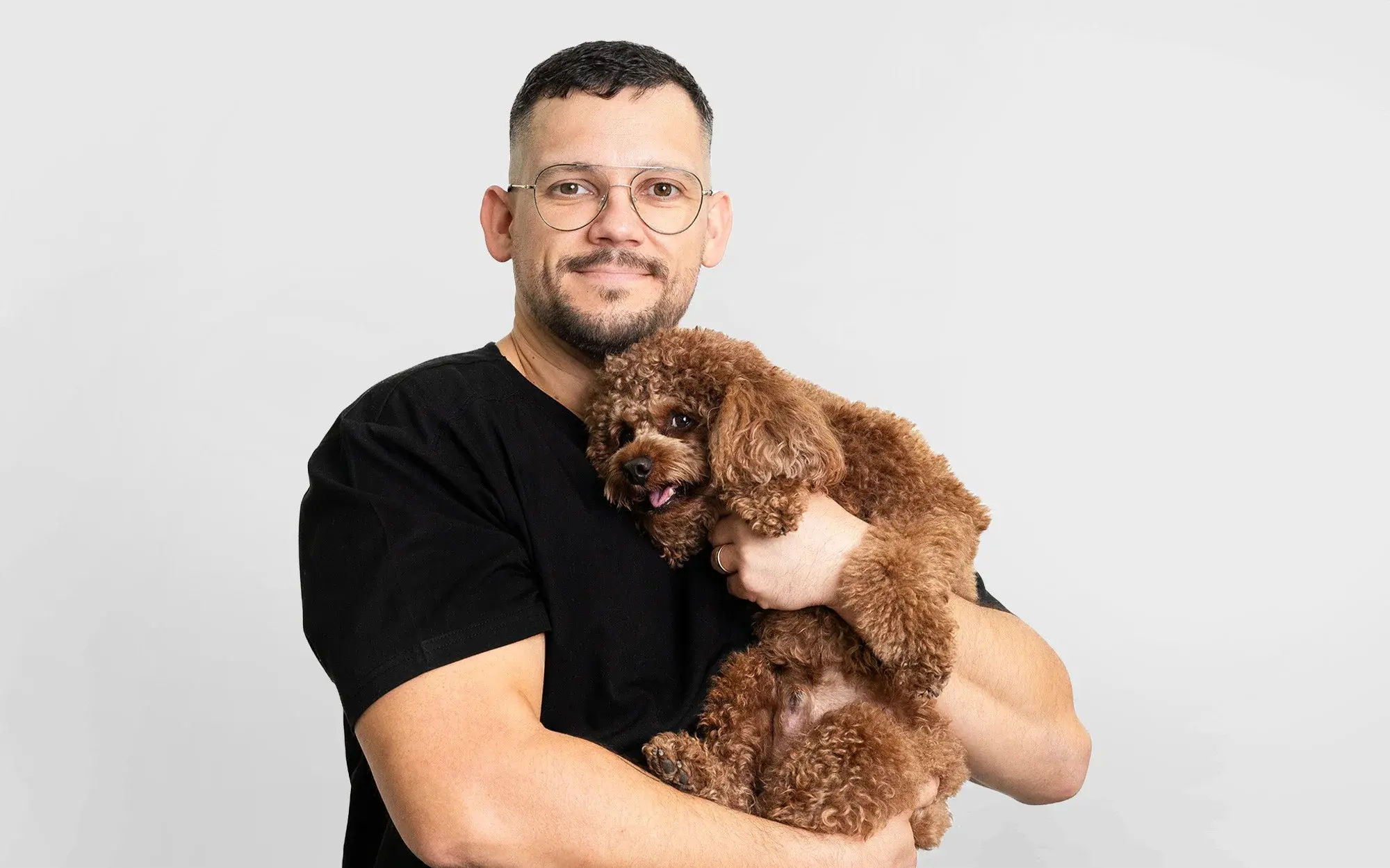 Dr. Rokas Proscevicius poses with a small brown dog, highlighting the caring bond between vet and pet at Noble Veterinary Clinic.