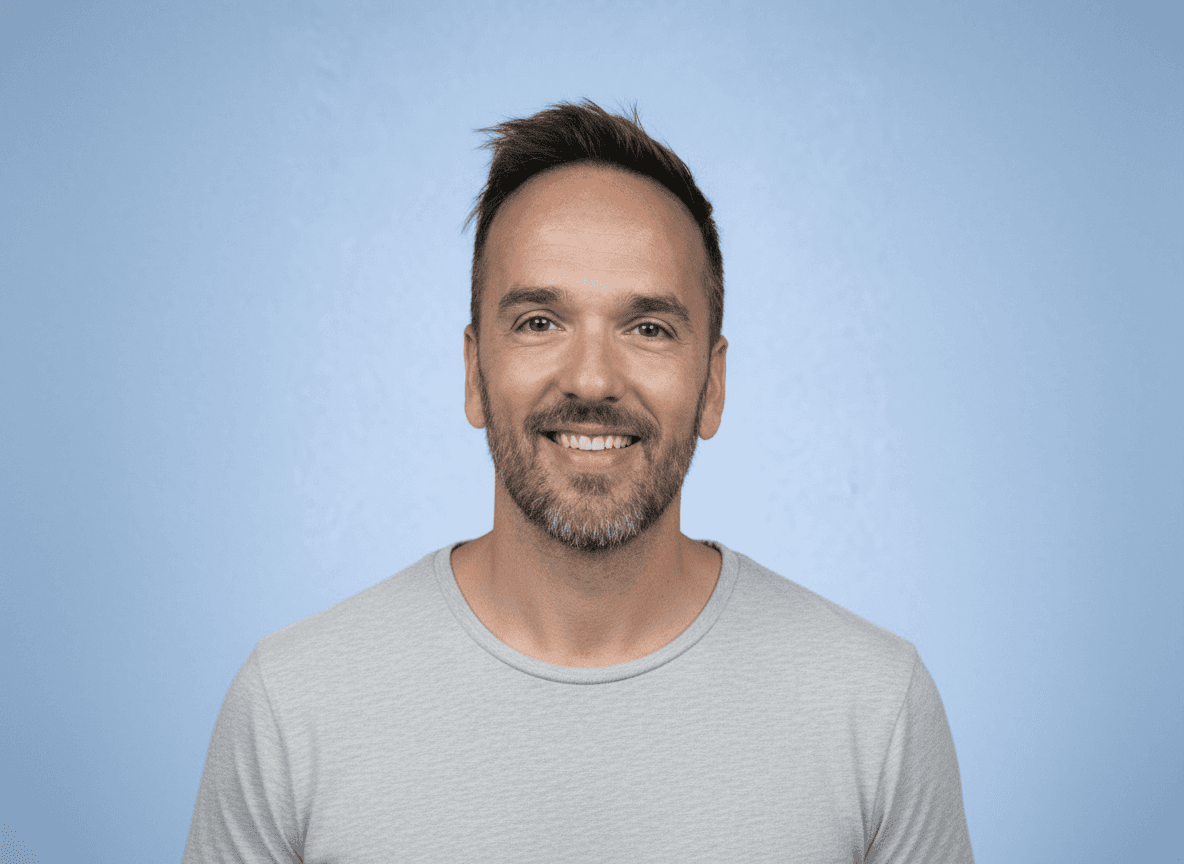 A man with curly hair and glasses looking at the camera