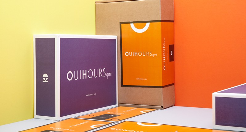 A set of purple white and orange card boxes put on a table near some orange papers with logos on them.