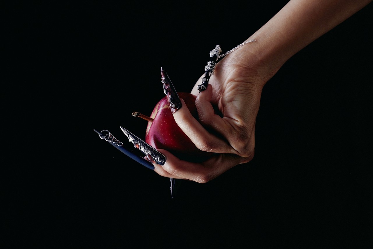 A hand with long nails holding a red apple in dramatic lighting.