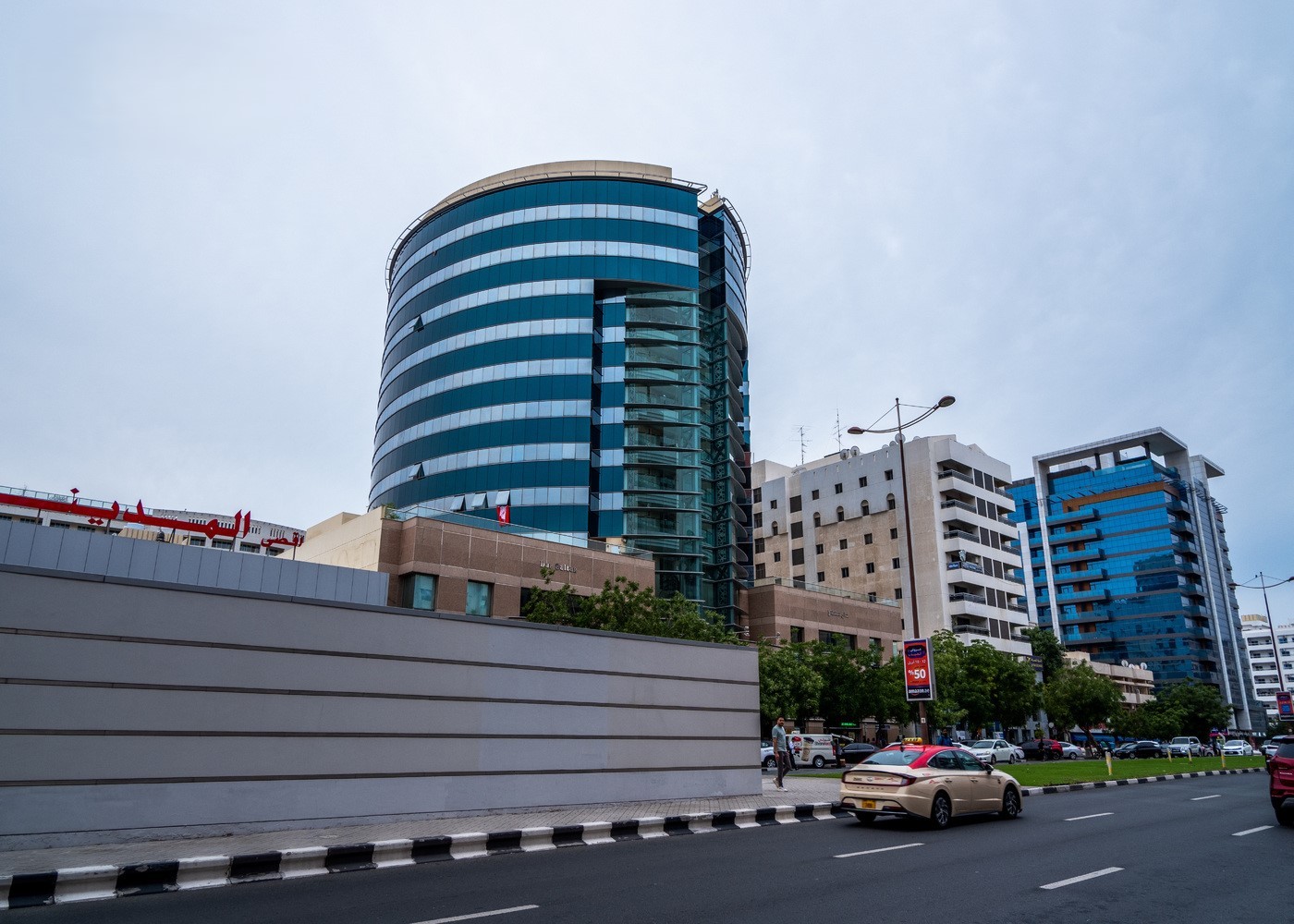 Modern street in Deira with glass buildings, cars, and pedestrians under an overcast sky, showing Dubai’s urban growth.