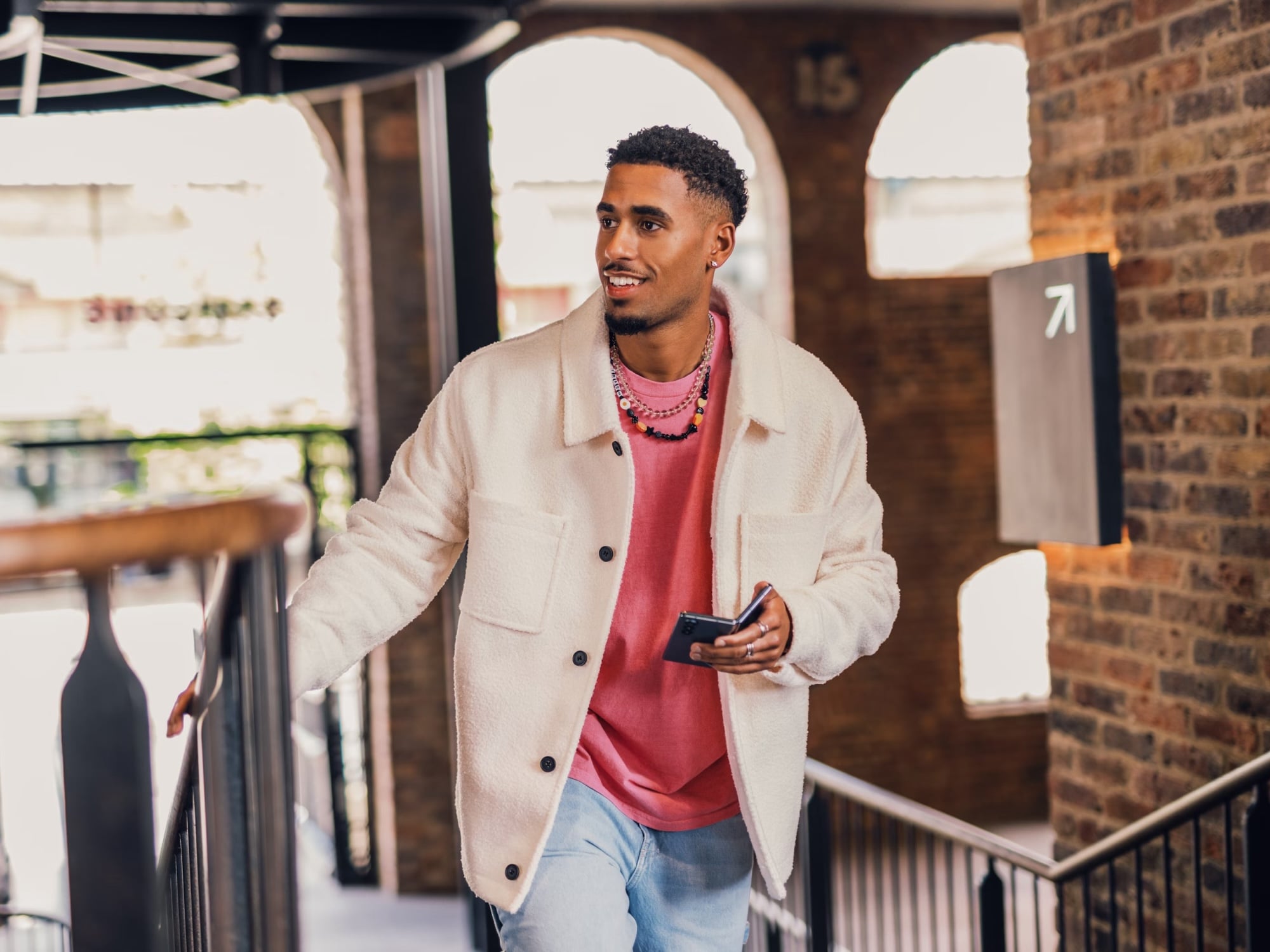 A young man walking the stairs of a building is smiling while holding his phone because he received a notification that money has been deposited back in his GoDutch bank account