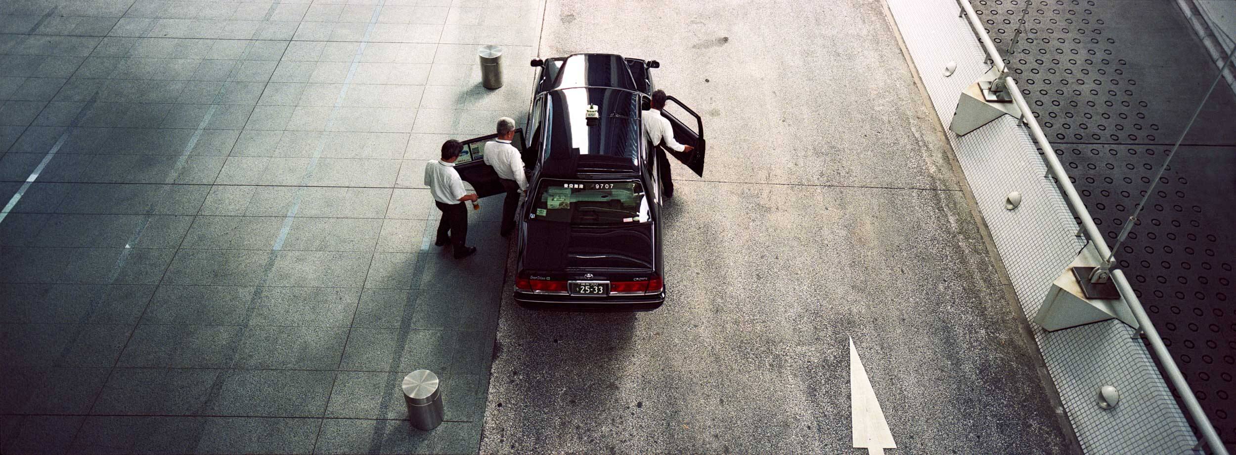 A typical Japanese taxi in Tokyo with three people entering in white shirts photographed on film with the Hasselblad XPan