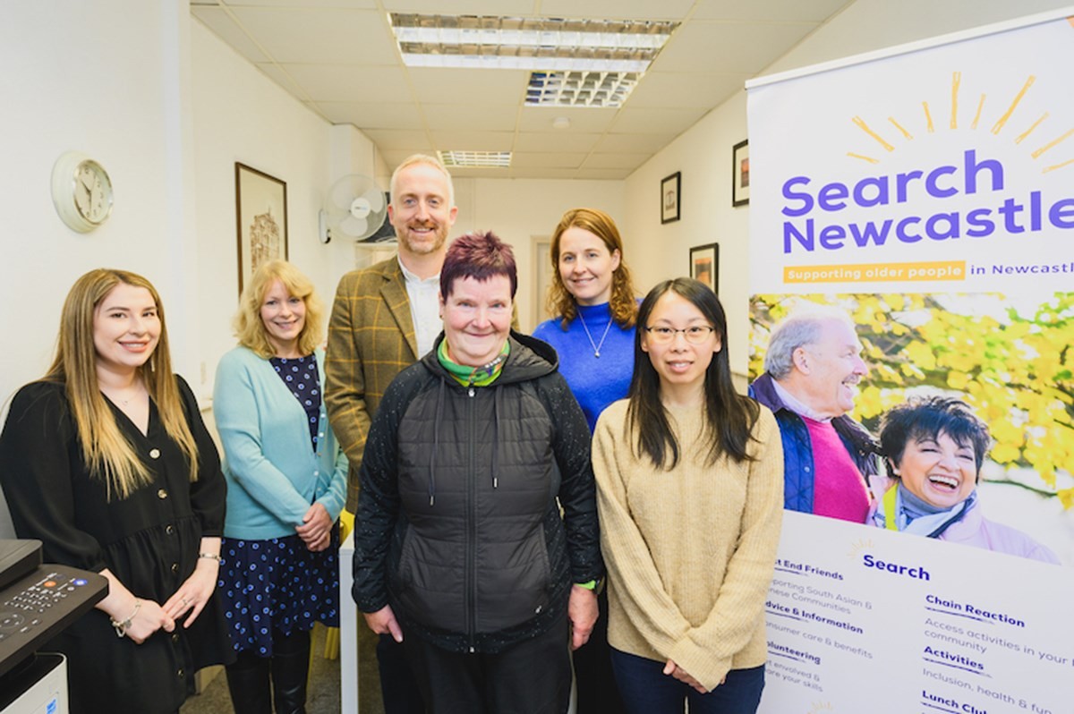 Group of six people standing indoors next to a banner that reads ‘Search Newcastle – Supporting older people in Newcastle.’