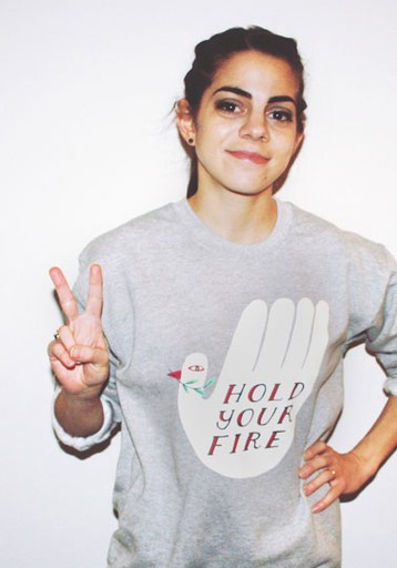Woman wearing "Hold Your Fire" sweatshirt making peace sign gesture.