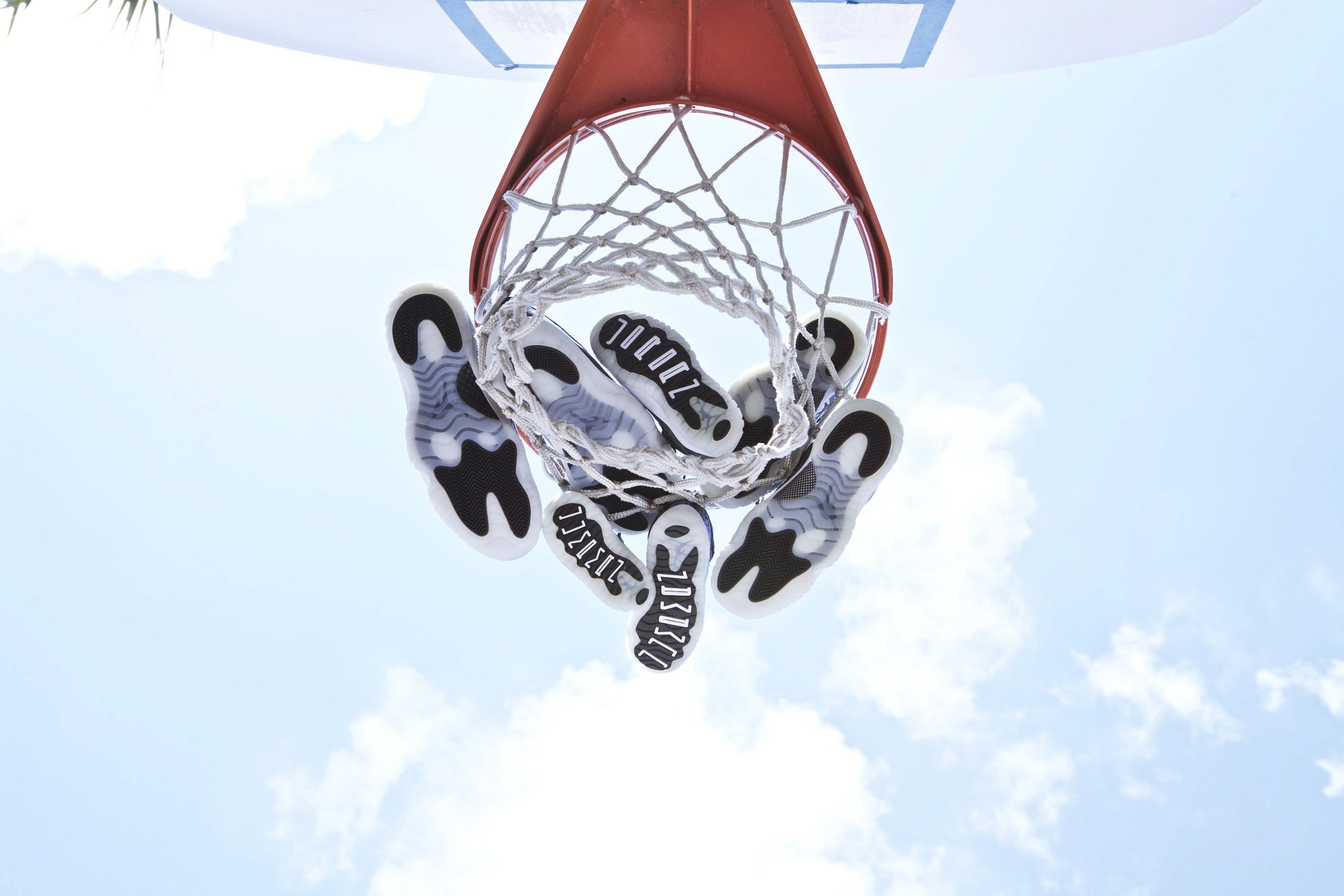 Sneakers hanging through an outdoor basketball hoop against a bright blue sky.