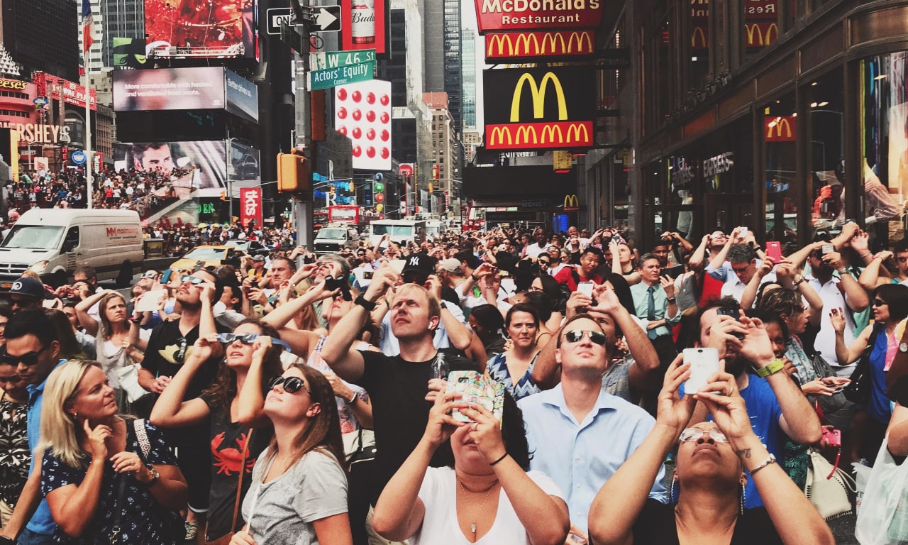 Large crowd in a busy city center looking up at digital billboards, representing mass reach and high-impact DOOH advertising.