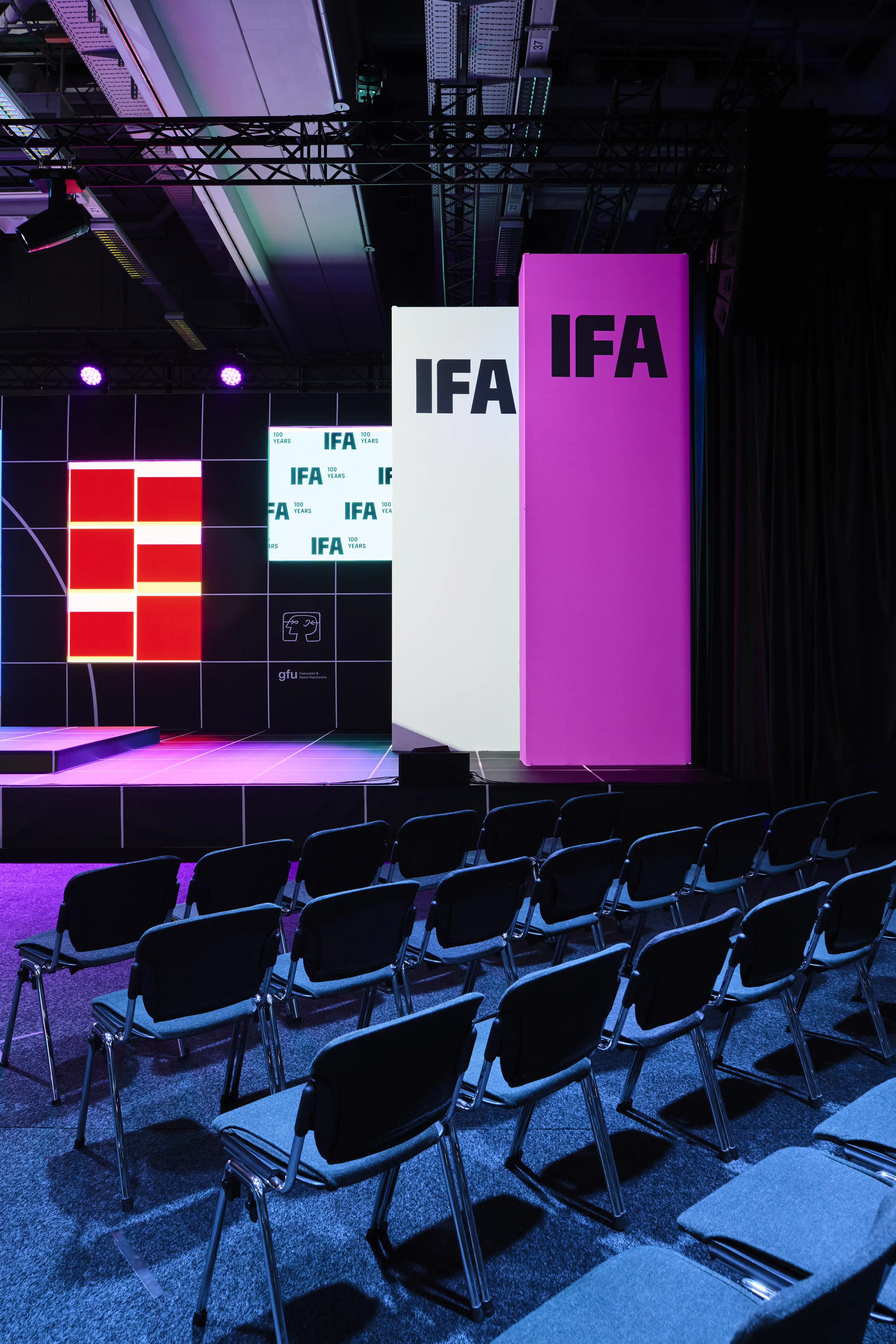 Stage view with white and magenta IFA pillars, red logo wall and rows of chairs.