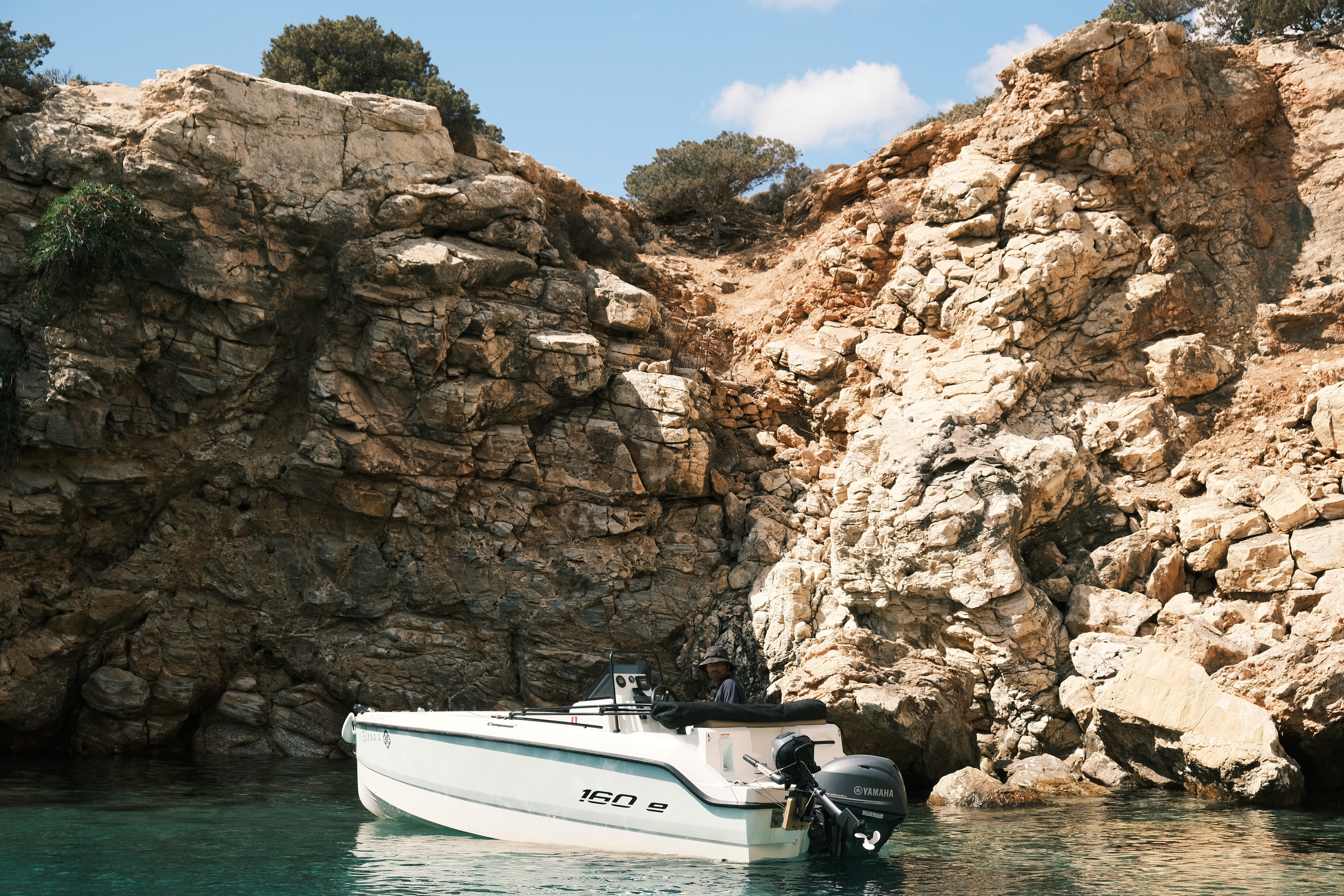 White Compass 16Oe yacht anchored in turquoise waters near dramatic limestone cliffs and rocky coastline of the Cyclades.