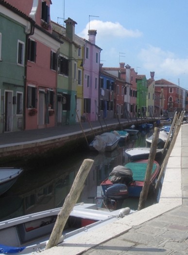 A photo of some colored houses and some covered boats sitting in a water canal.