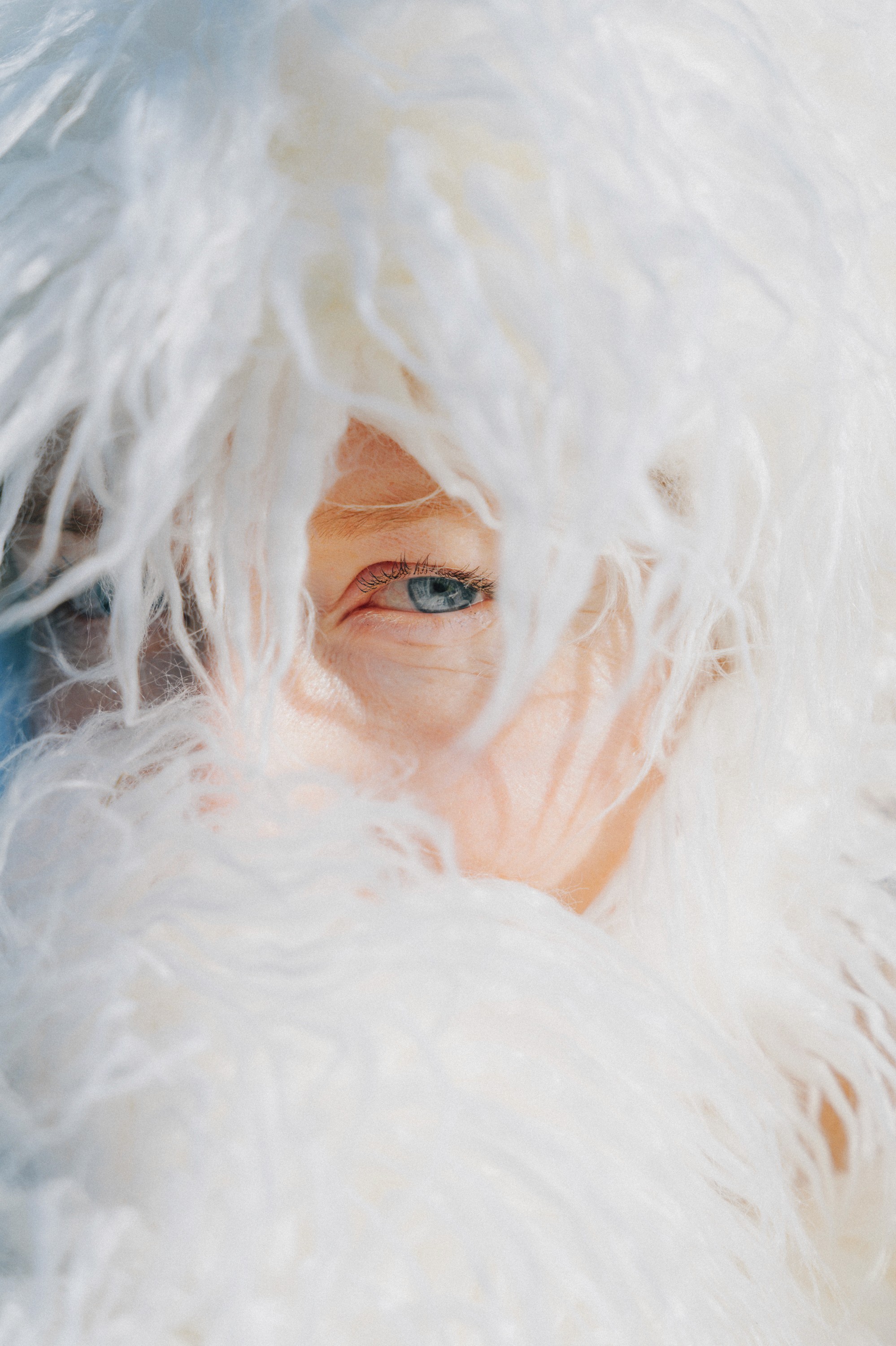 Portrait no.2 of Creature Zero by Ásta Fanney Sigurðardóttir, a close-up of a face peering through a curtain of soft white strands, one blue eye visible.