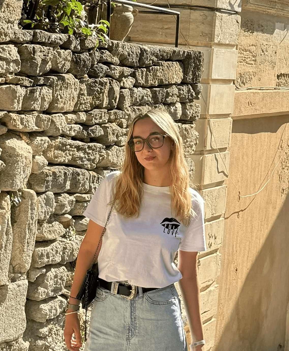 Femme blonde en lunettes et t-shirt blanc dans une ruelle en pierre, portrait de voyage