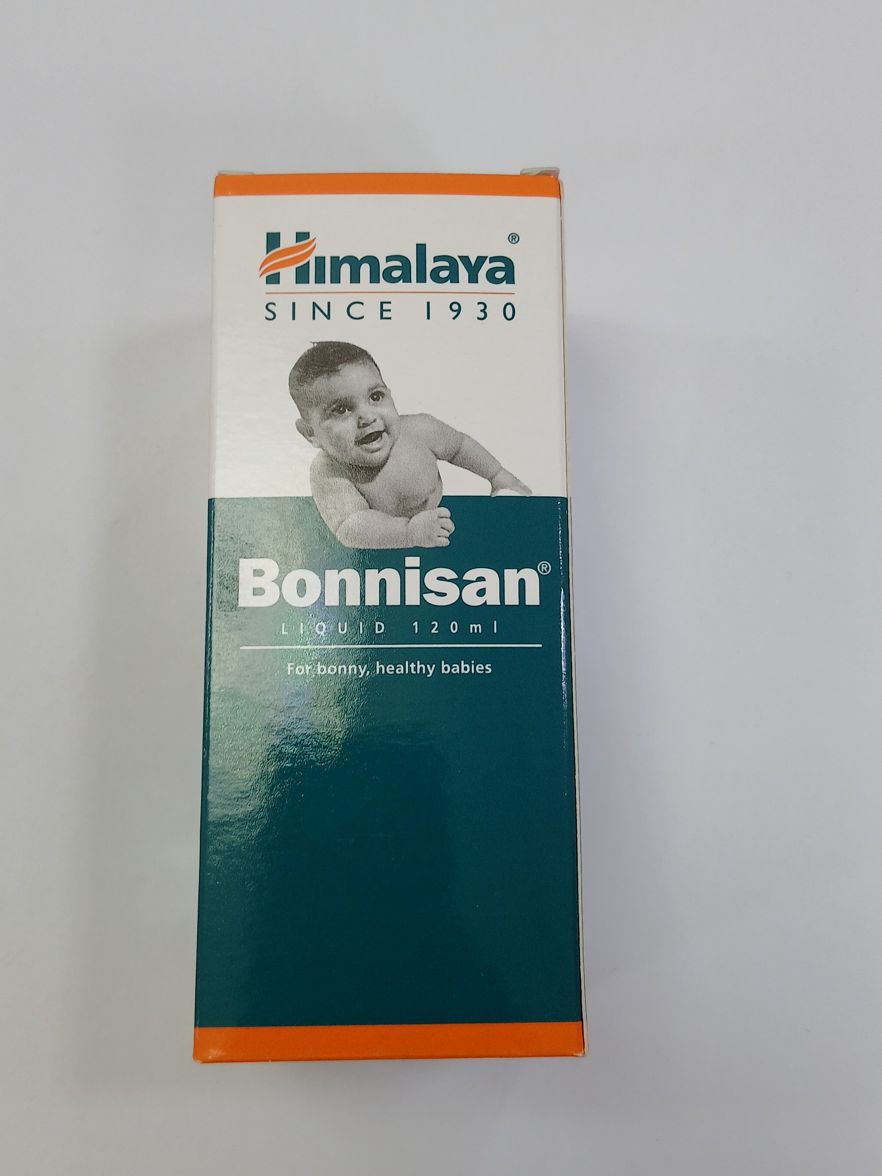 White and orange cardboard box packaging with a black and white photograph of a baby lying on its back, set against a teal background with text in white and orange.